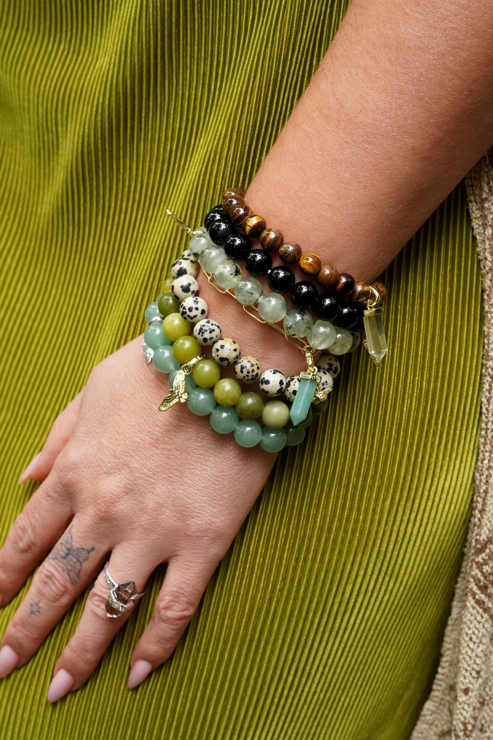 Close-up of a wrist wearing multiple gemstone beaded bracelets on a green fabric background