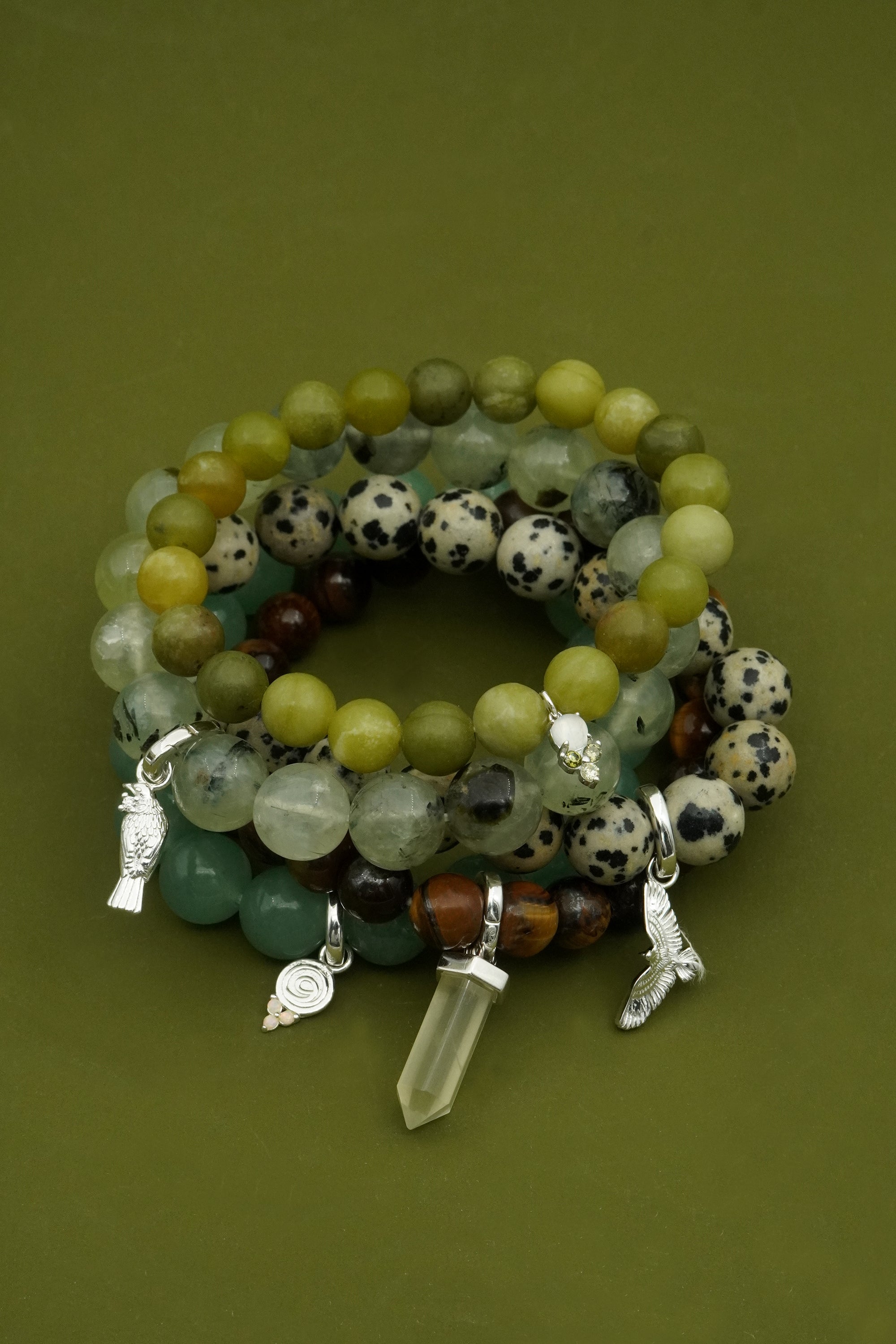 Stack of green beaded spiritual NZ gemstone bracelets with crystal pendants on a green background