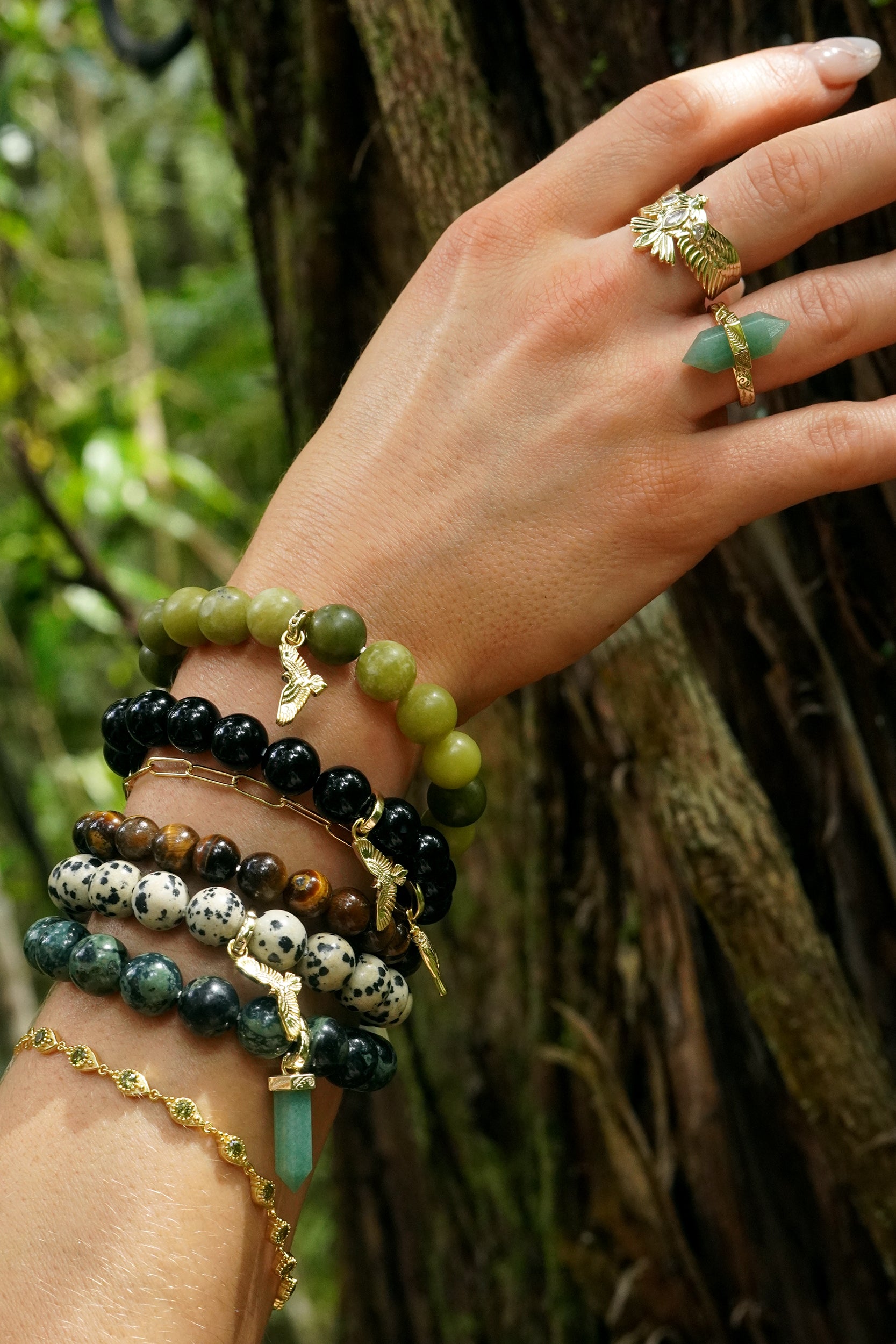 Hand wearing multiple green spiritual beaded bracelets with a forest background