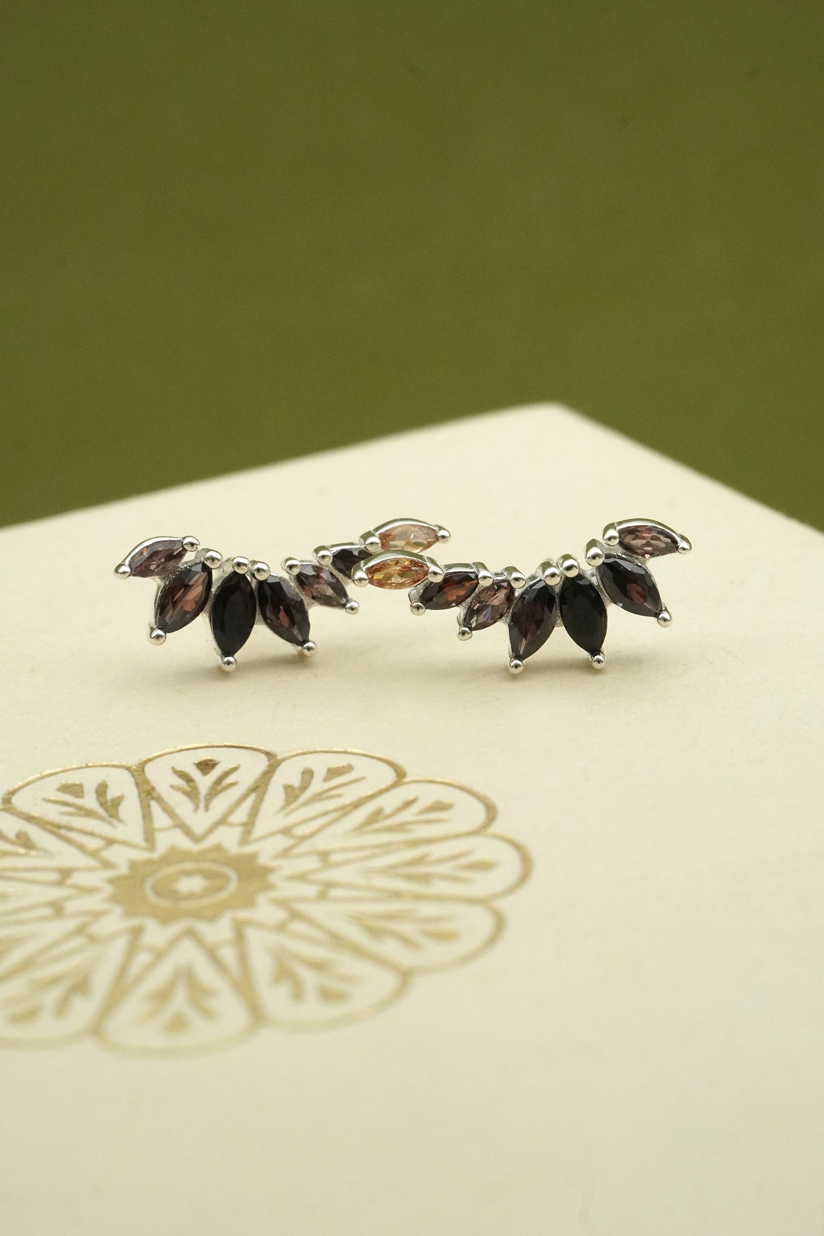 Silver earring with marquise-shaped gemstones on a light green background