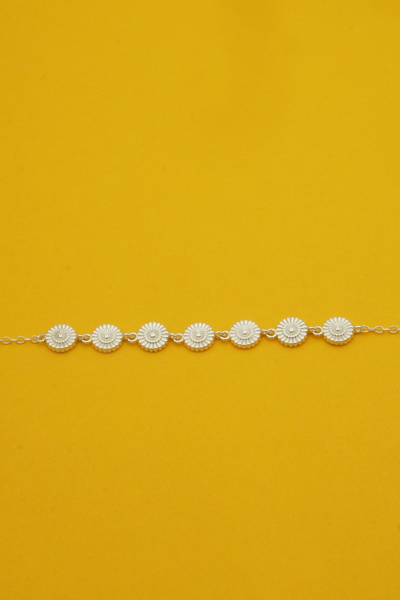 Silver flower bracelet with daisy designs on a bright yellow background