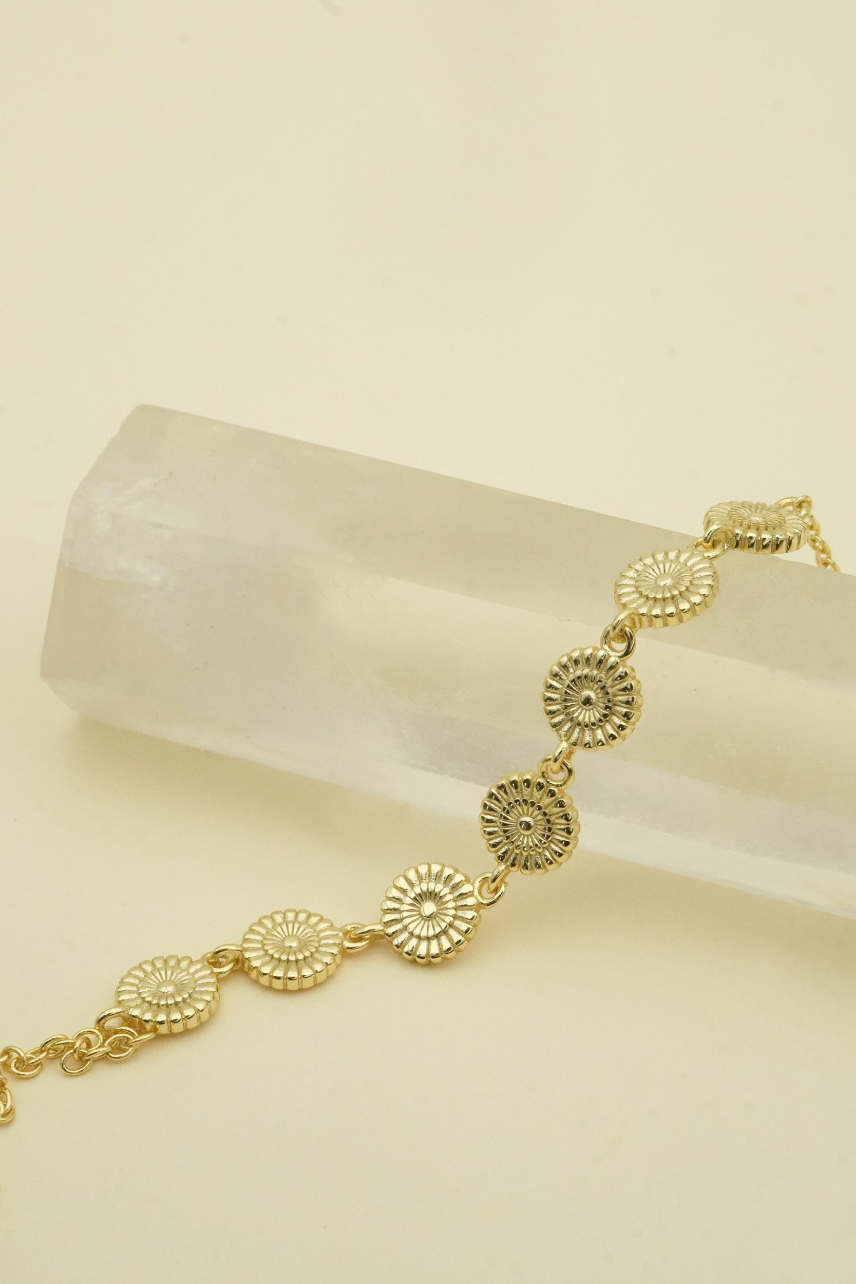 Gold bracelet with circular designs on a beige background