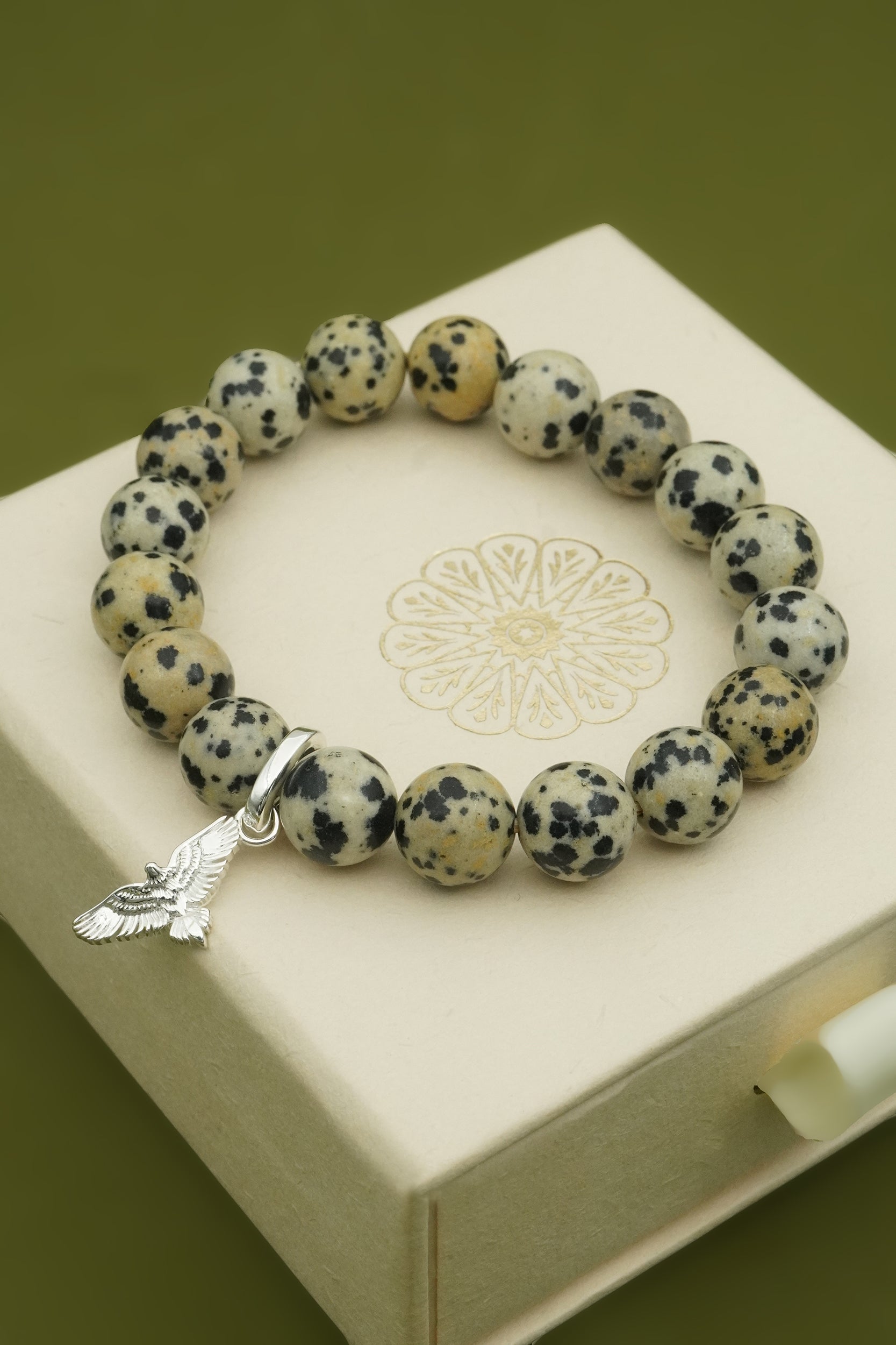 Bracelet with dalmatian jasper beads and a silver hawk bird charm on a white box with a floral design.