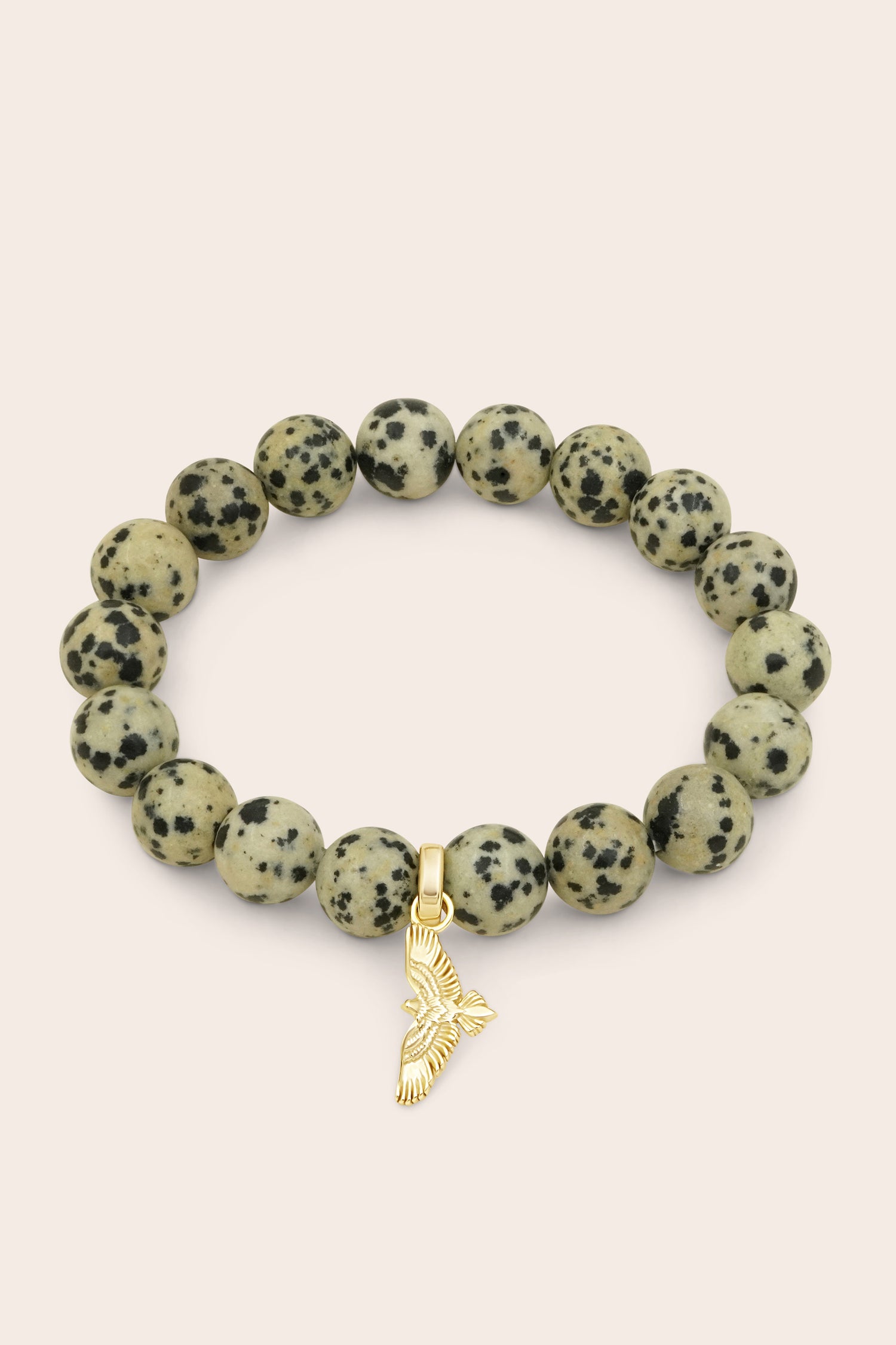 Bracelet with dalmatian jasper beads and a gold soar hawk bird charm on a light pink background