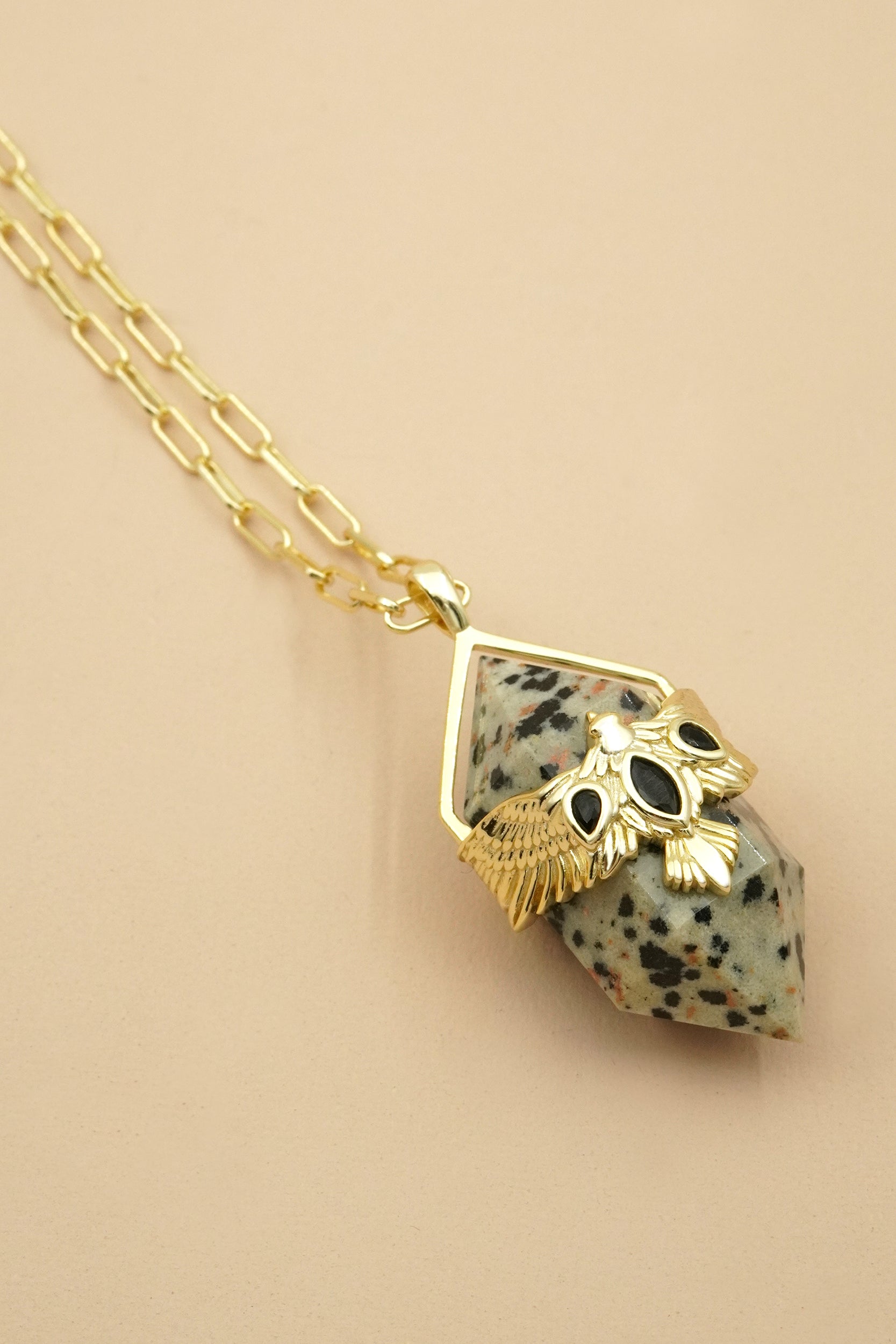 Necklace with a gold pendant featuring a speckled stone and eagle bird on a beige background