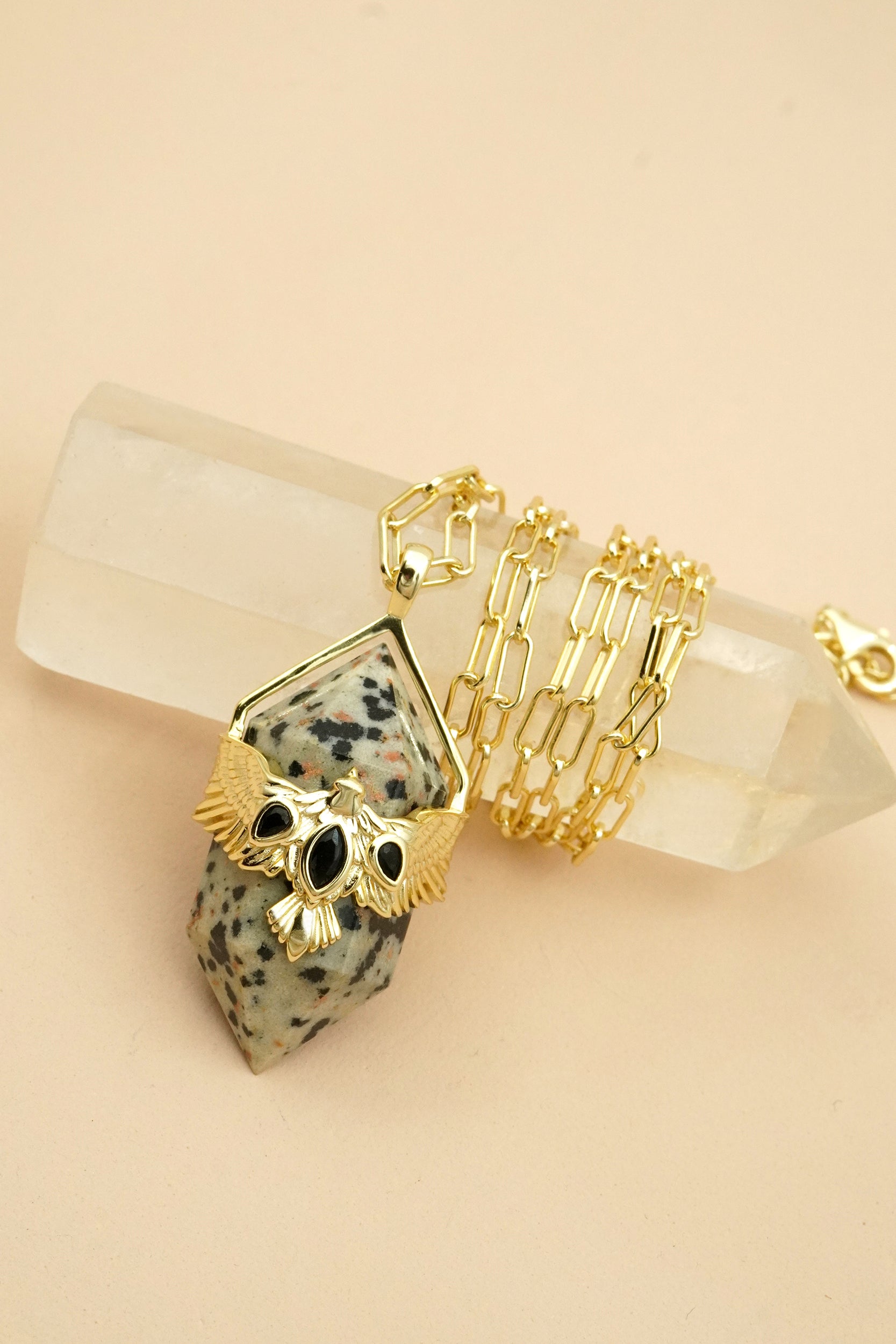 Gold necklace with gemstone pendant featuring a hawk bird with wings outstretched on a beige background