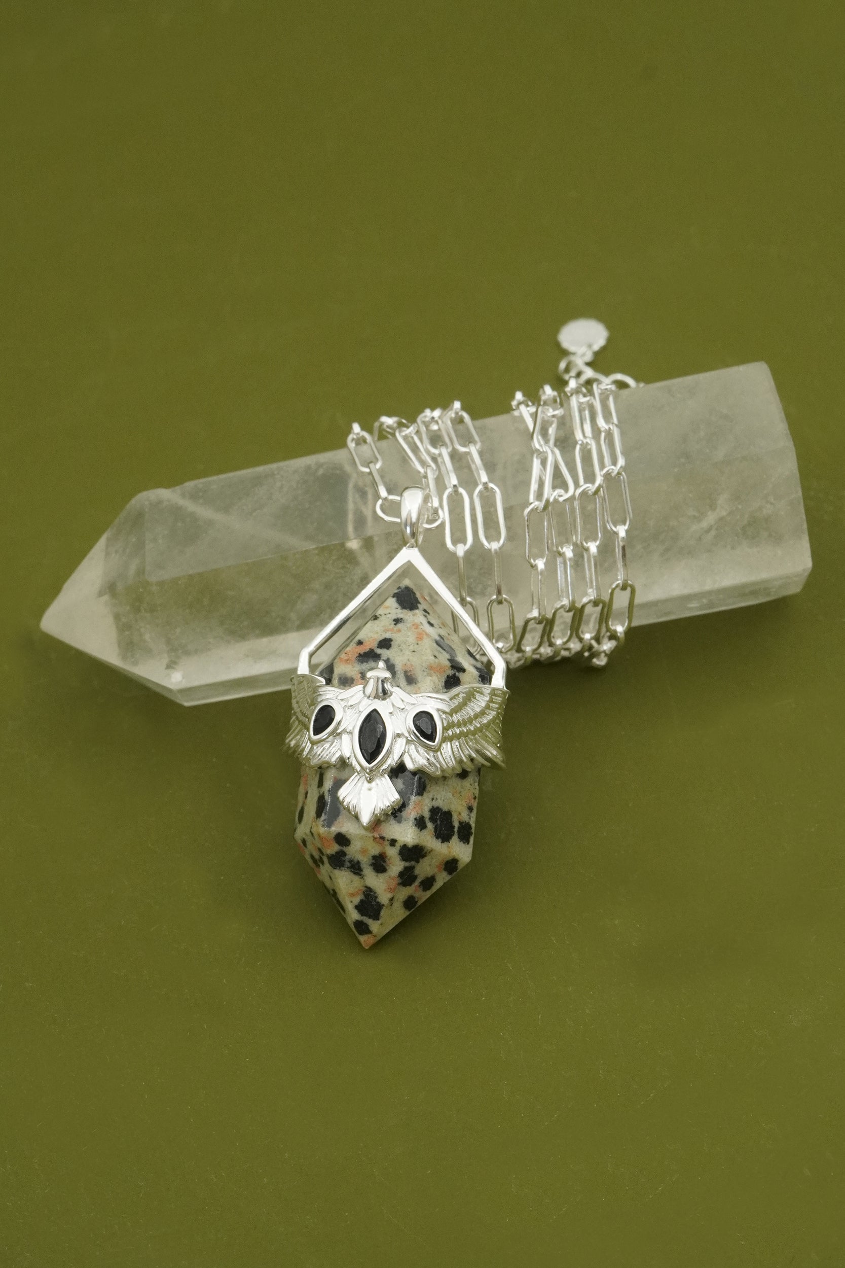 Silver jewellery set with bird pendant and on a crystal on a green background