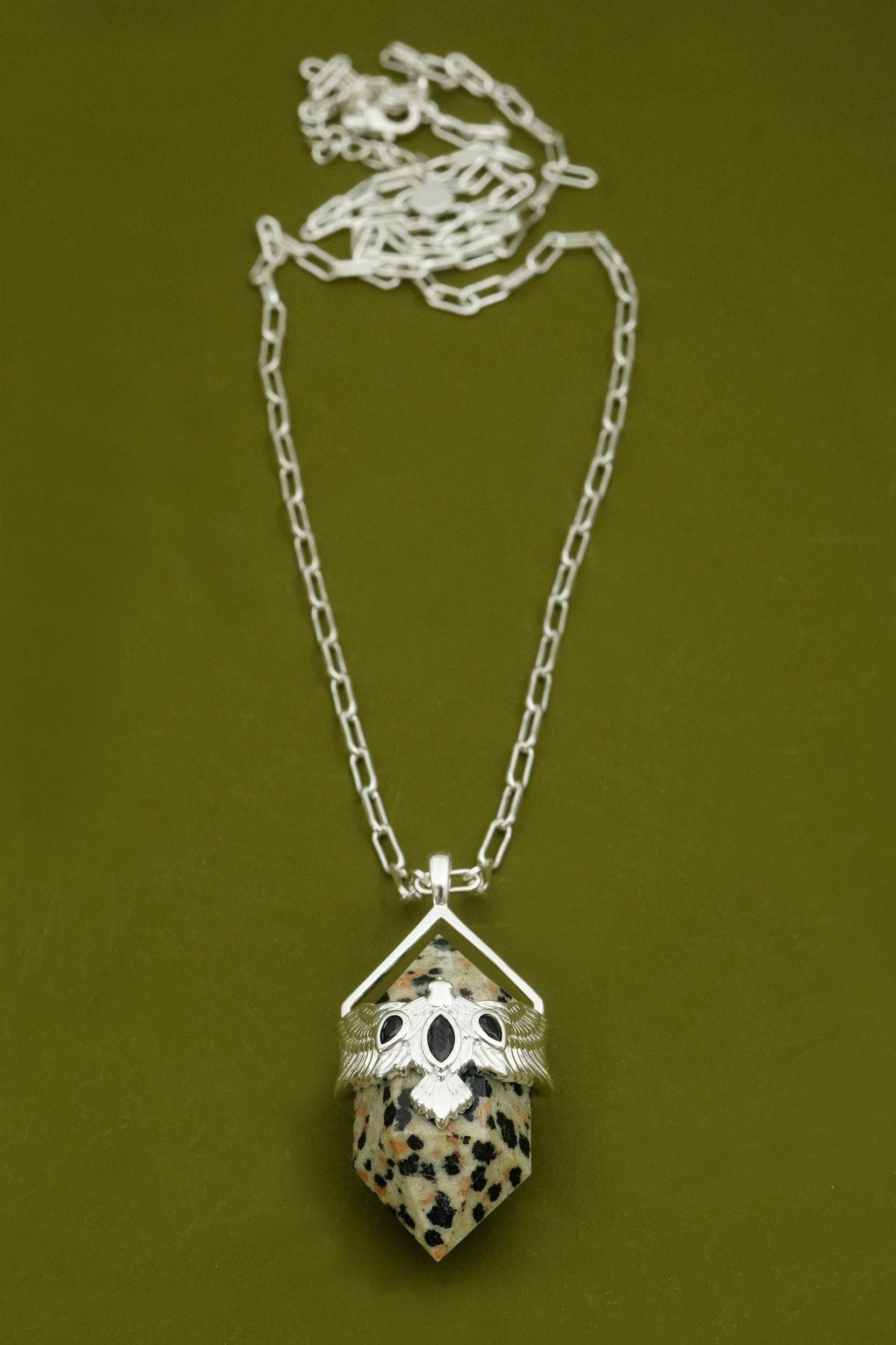 Silver Necklace with a dalmatian jasper stone pendant and NZ bird design on a green background