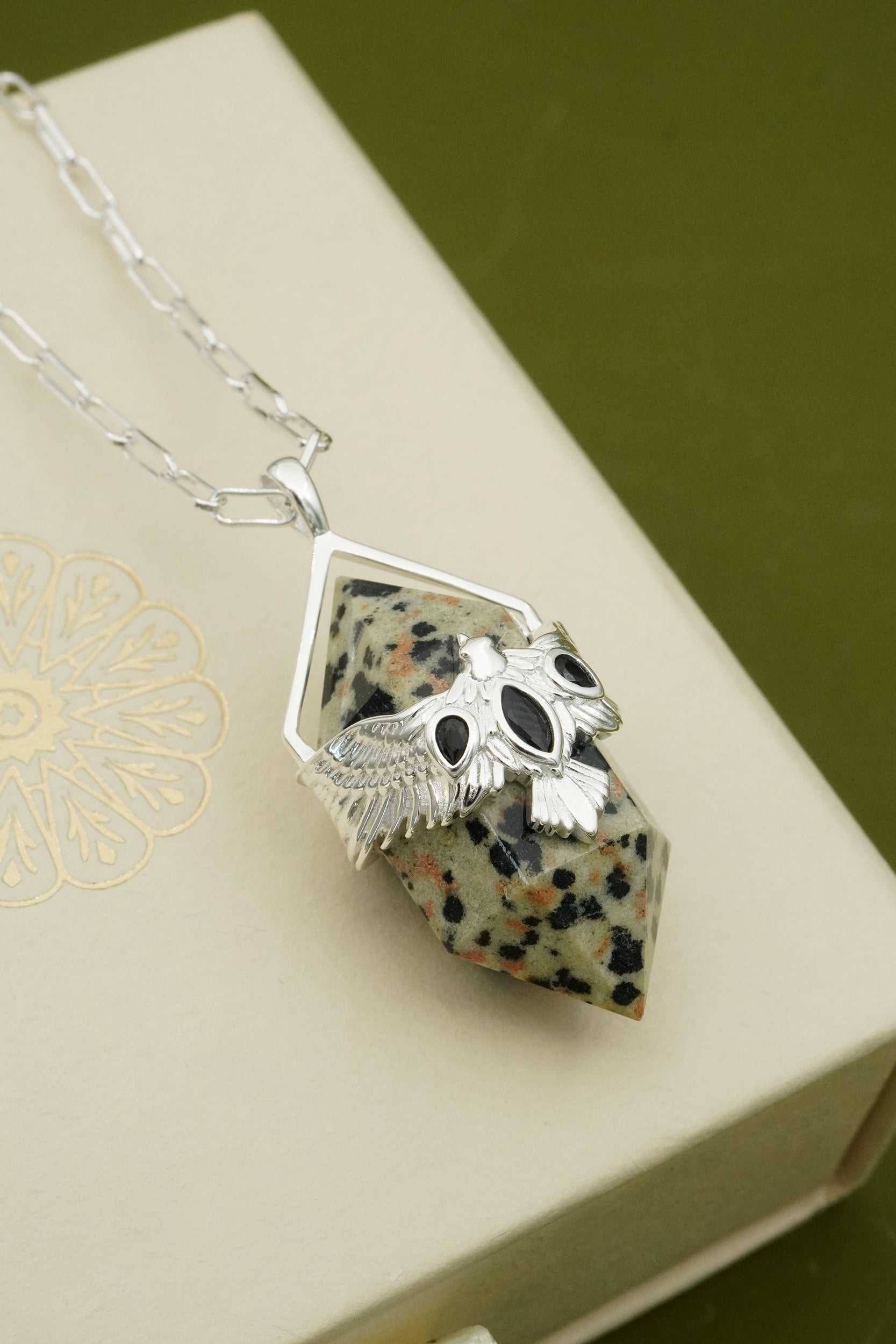 Silver hawk bird pendant on a stone with a green background