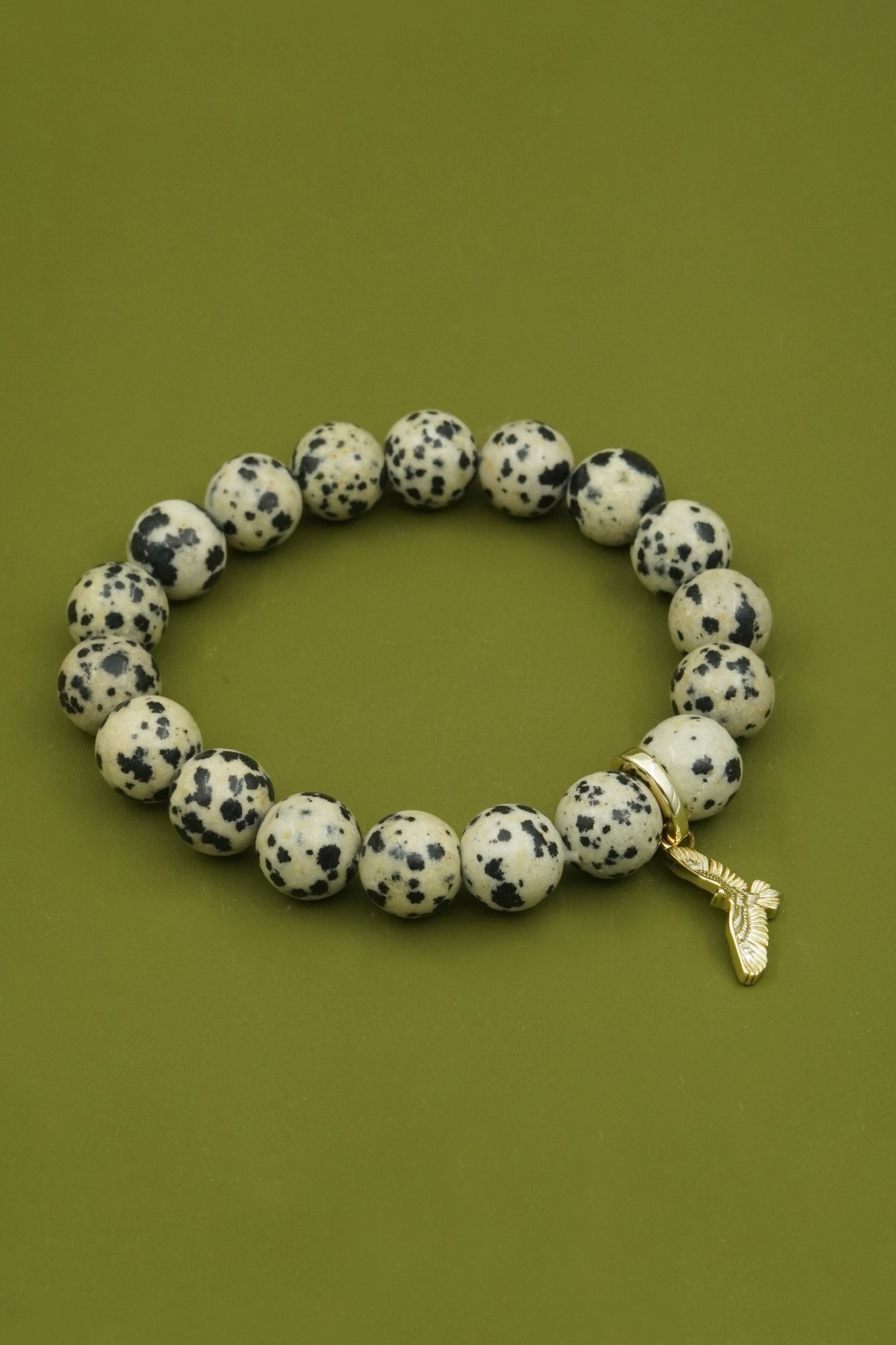 Beaded bracelet with dalmatian jasper stones and a gold bird charm on a green background