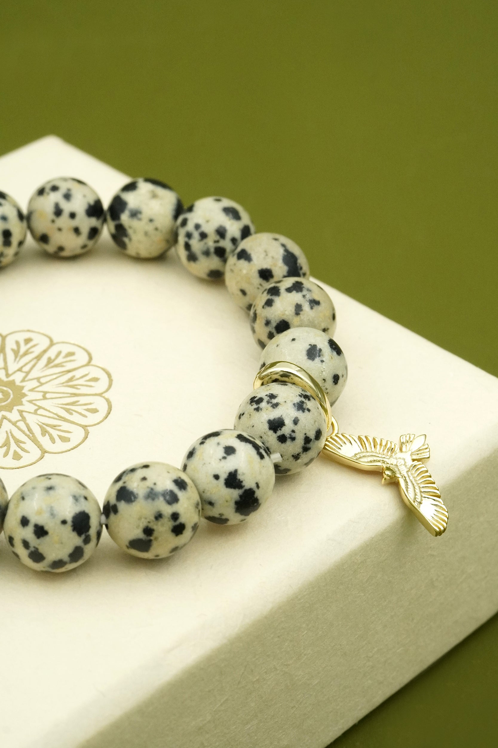Crystal Bracelet with dalmatian jasper beads and a gold Hawk Eagle  charm on a white box with a green background