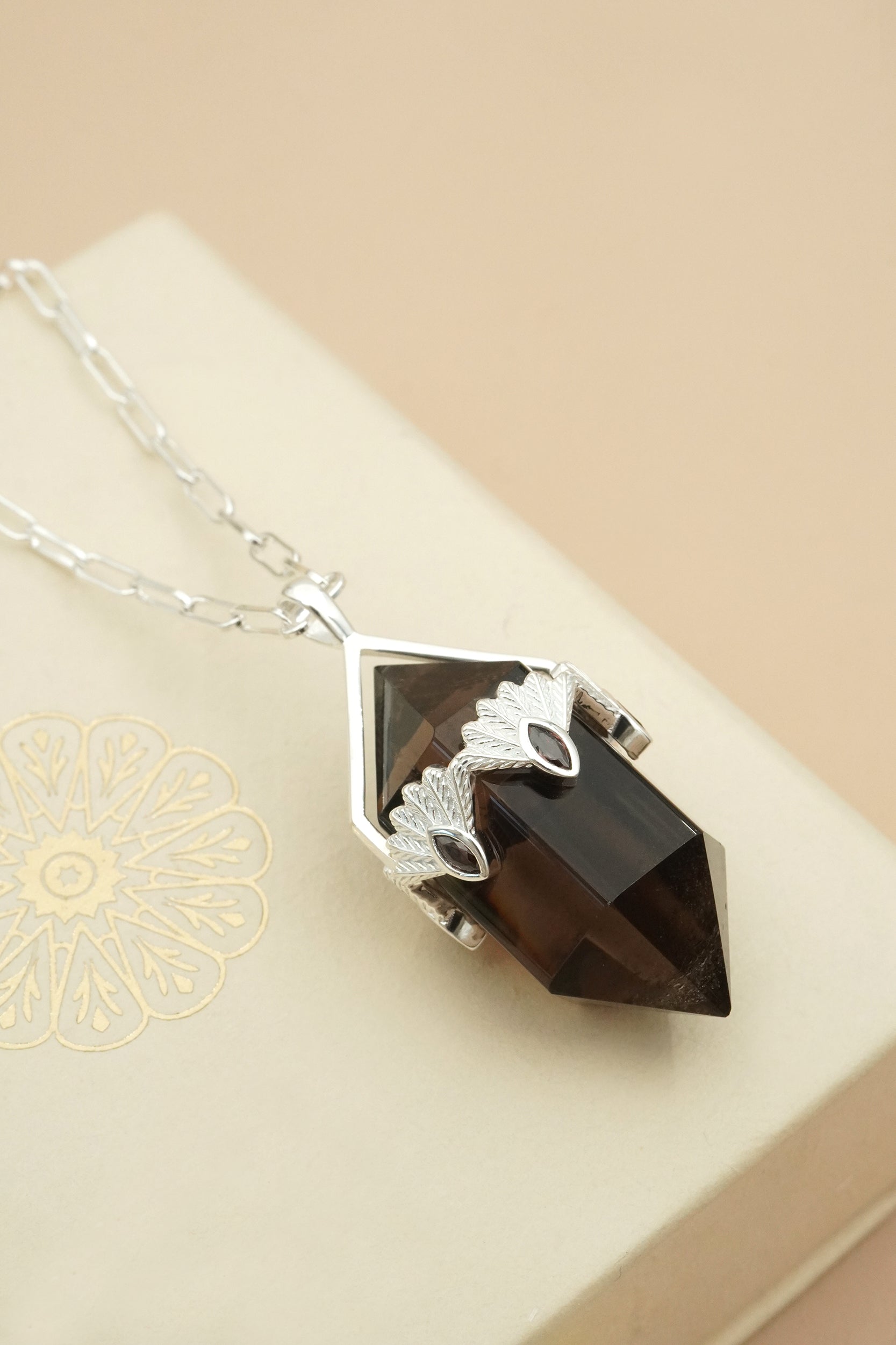 Smoky quartz crystal necklace with silver fantail piwakawaka setting on a beige background