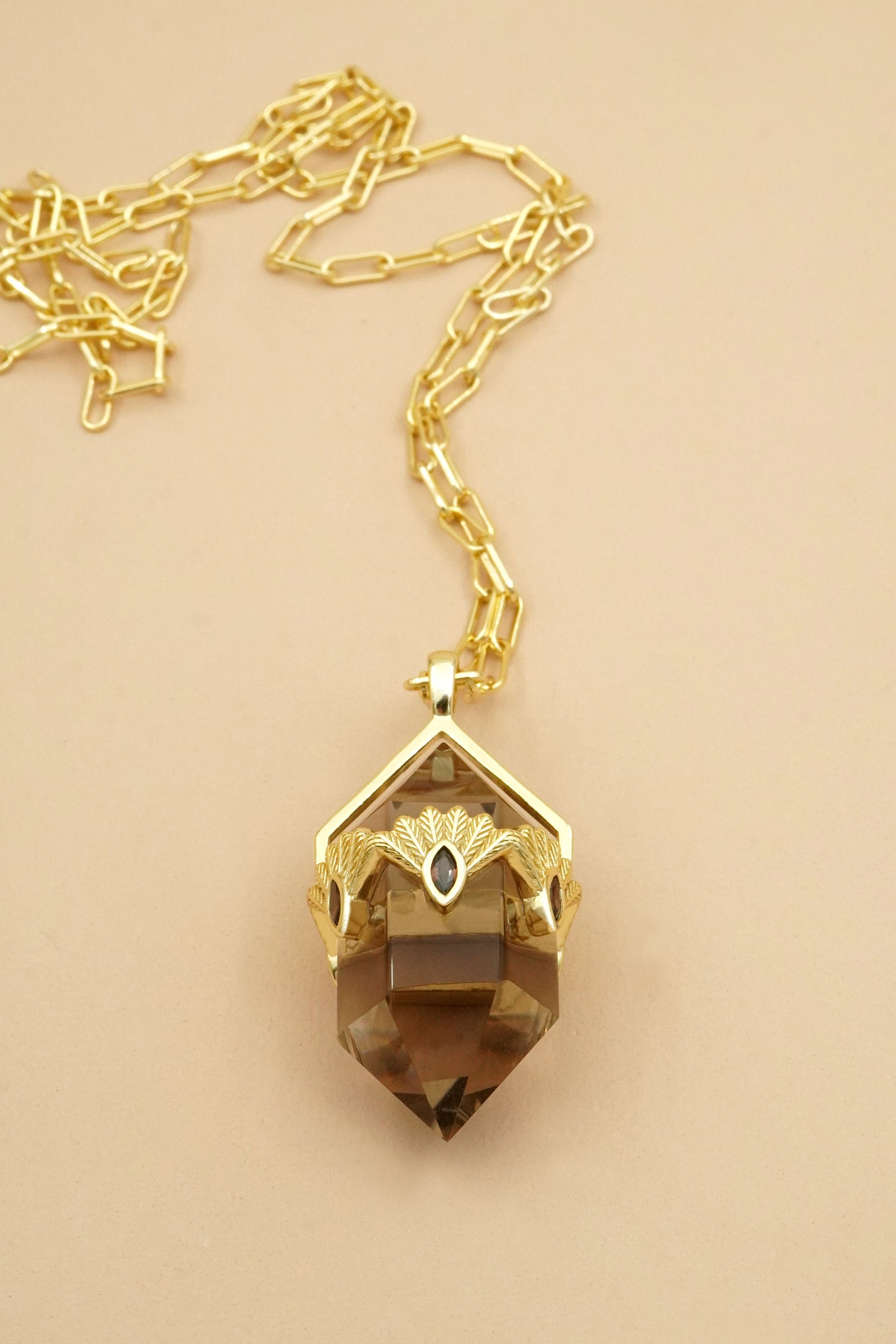 Gold fantail bird necklace with a smoky quartz pendant on a beige background