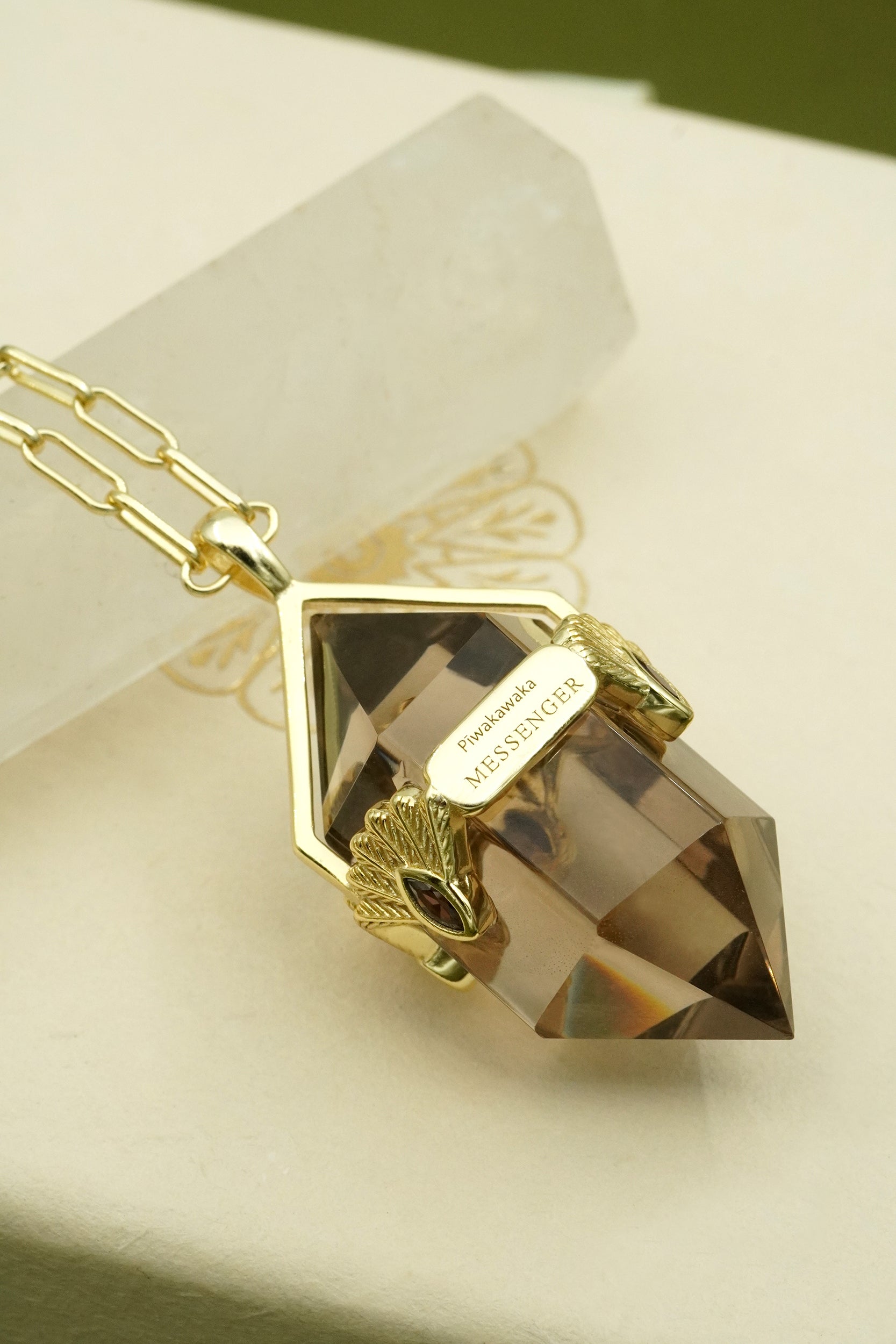 Gold fantail messenger spiritual necklace with a large smoky crystal pendant on a white surface