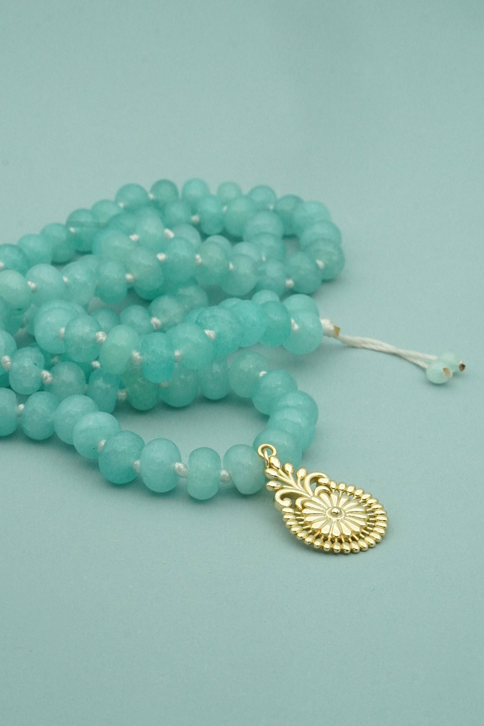 Turquoise beaded necklace with a gold flower pendant on a light blue background