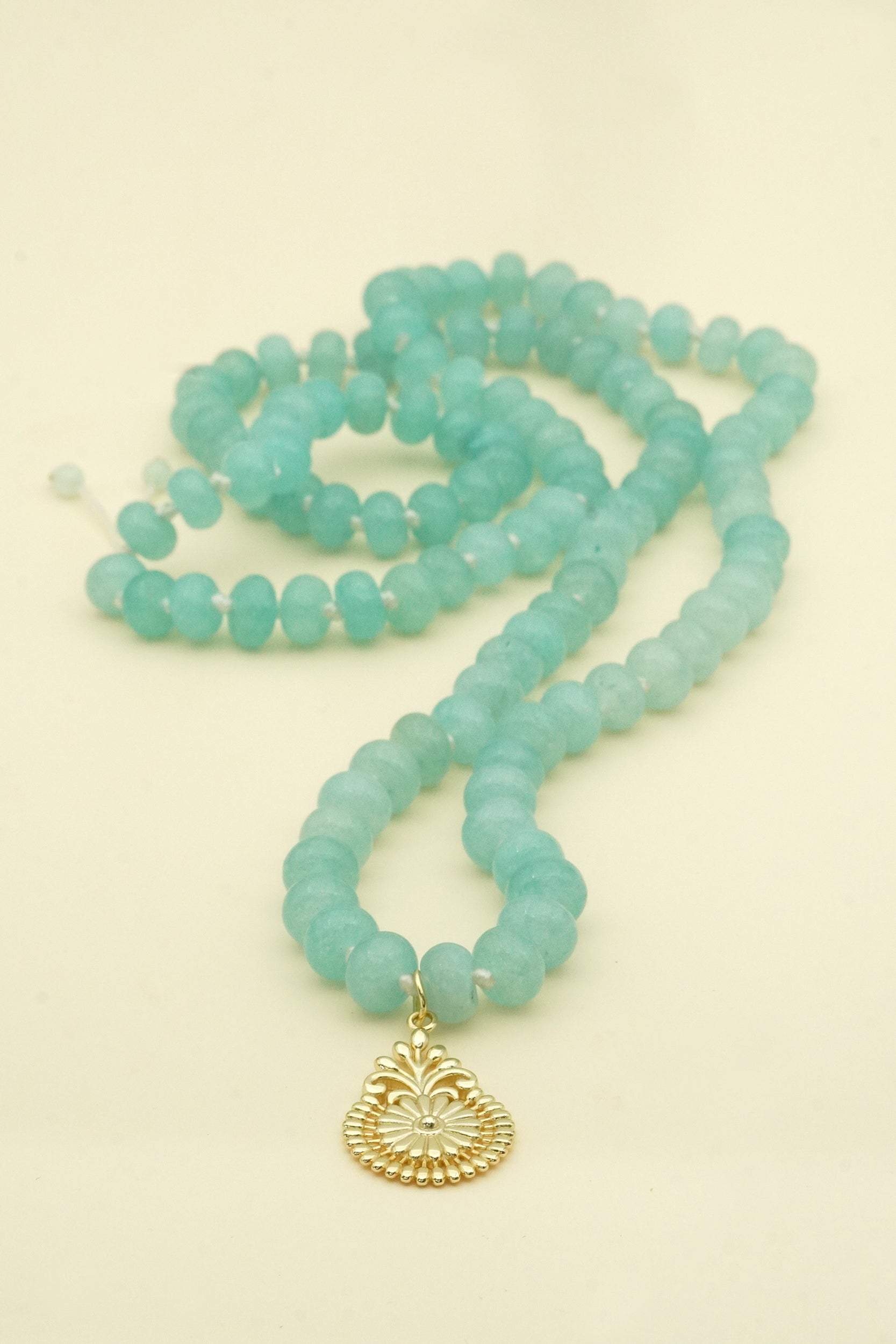 Turquoise aquamarine beaded mala necklace with a gold pendant on a beige background