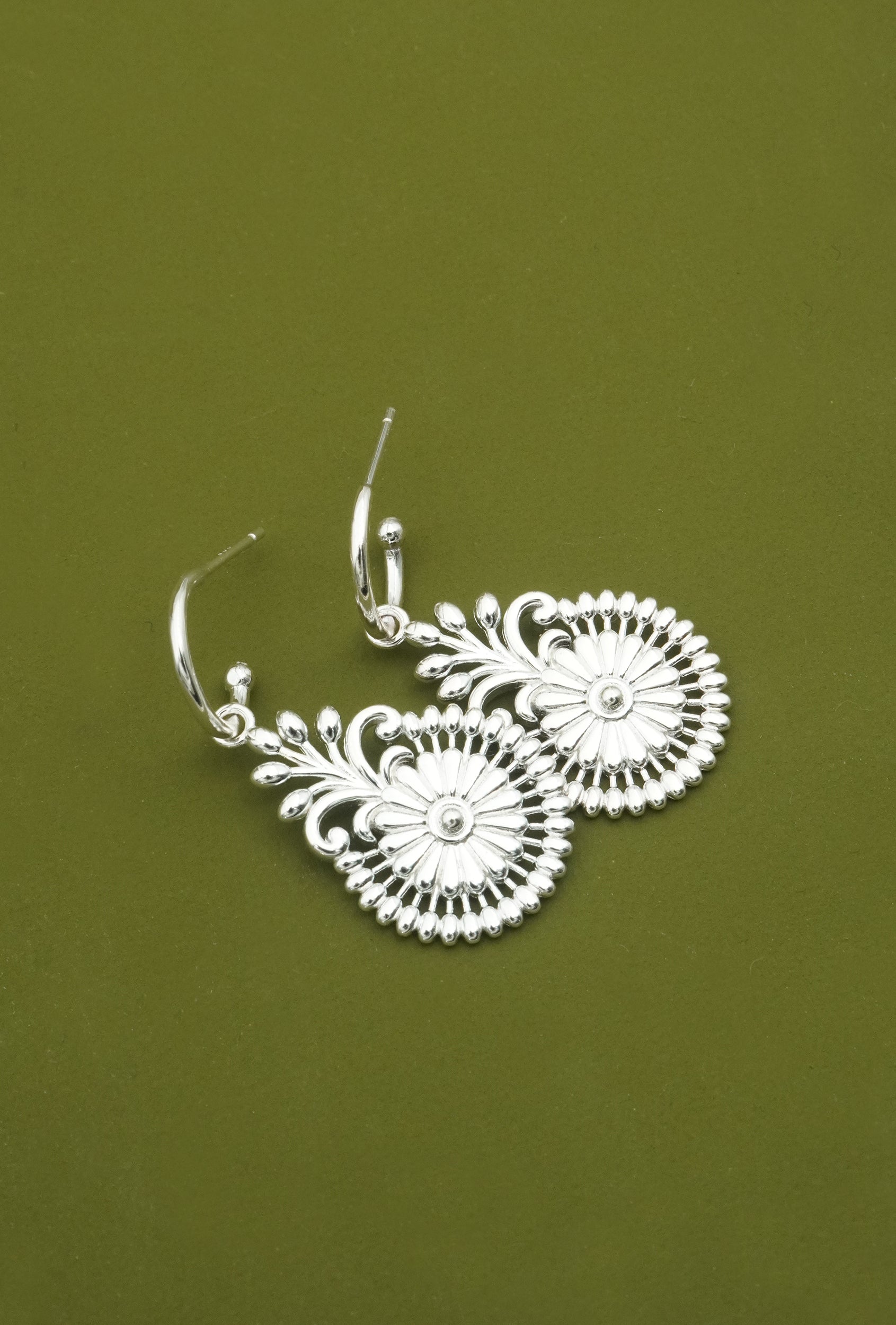 Silver statement floral earrings on a green background