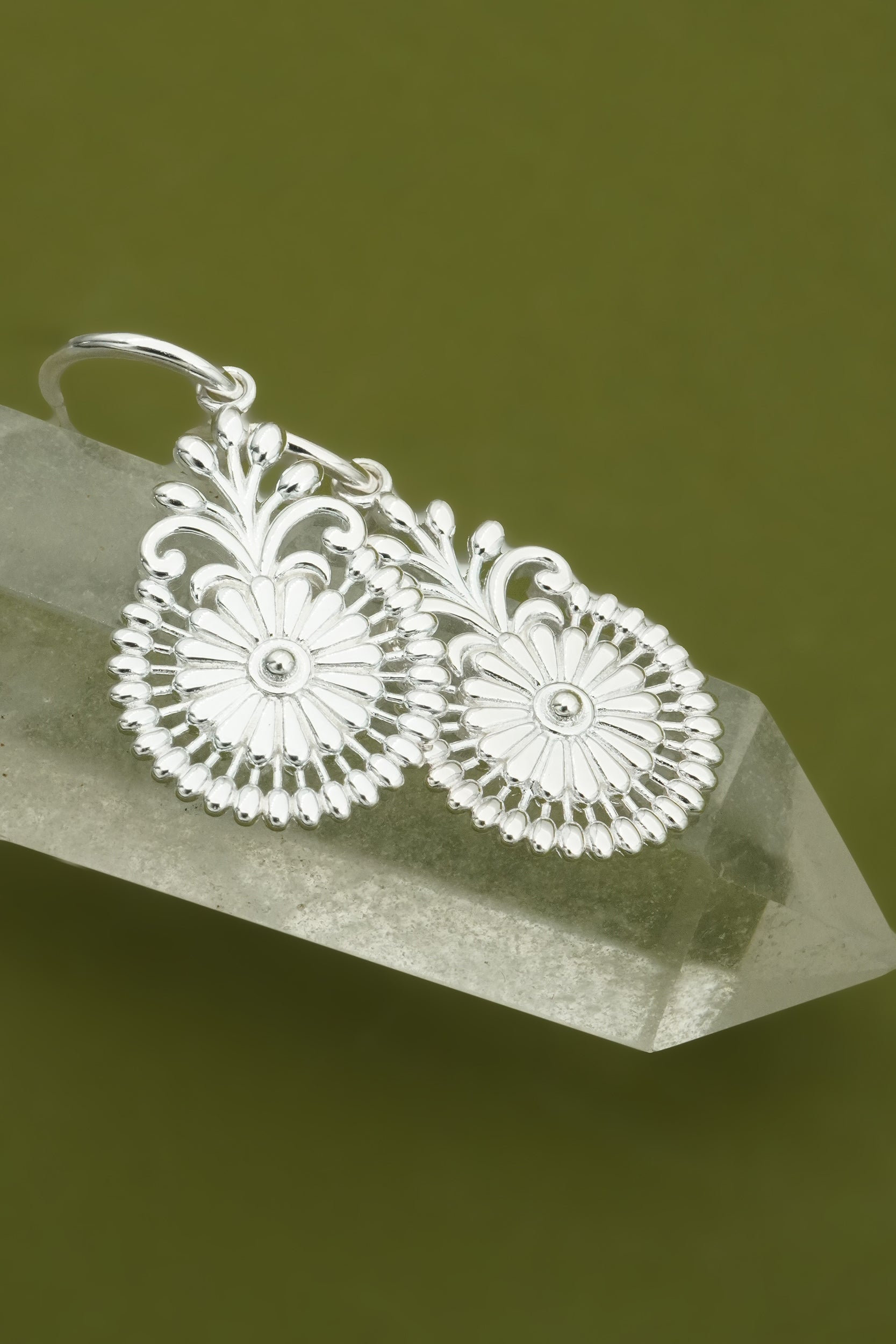 Silver flower earrings on a clear crystal with a green background