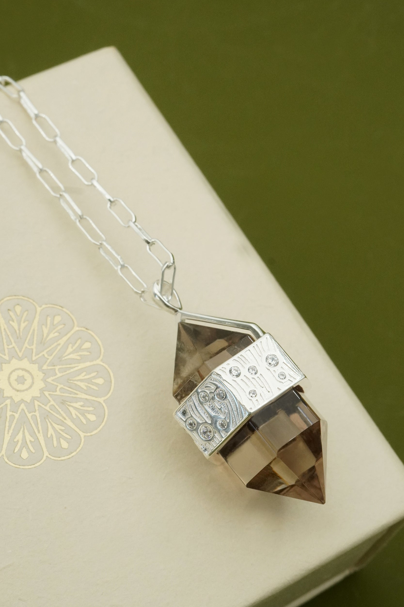Smoky quartz pendant on a silver chain with a decorative box in the background