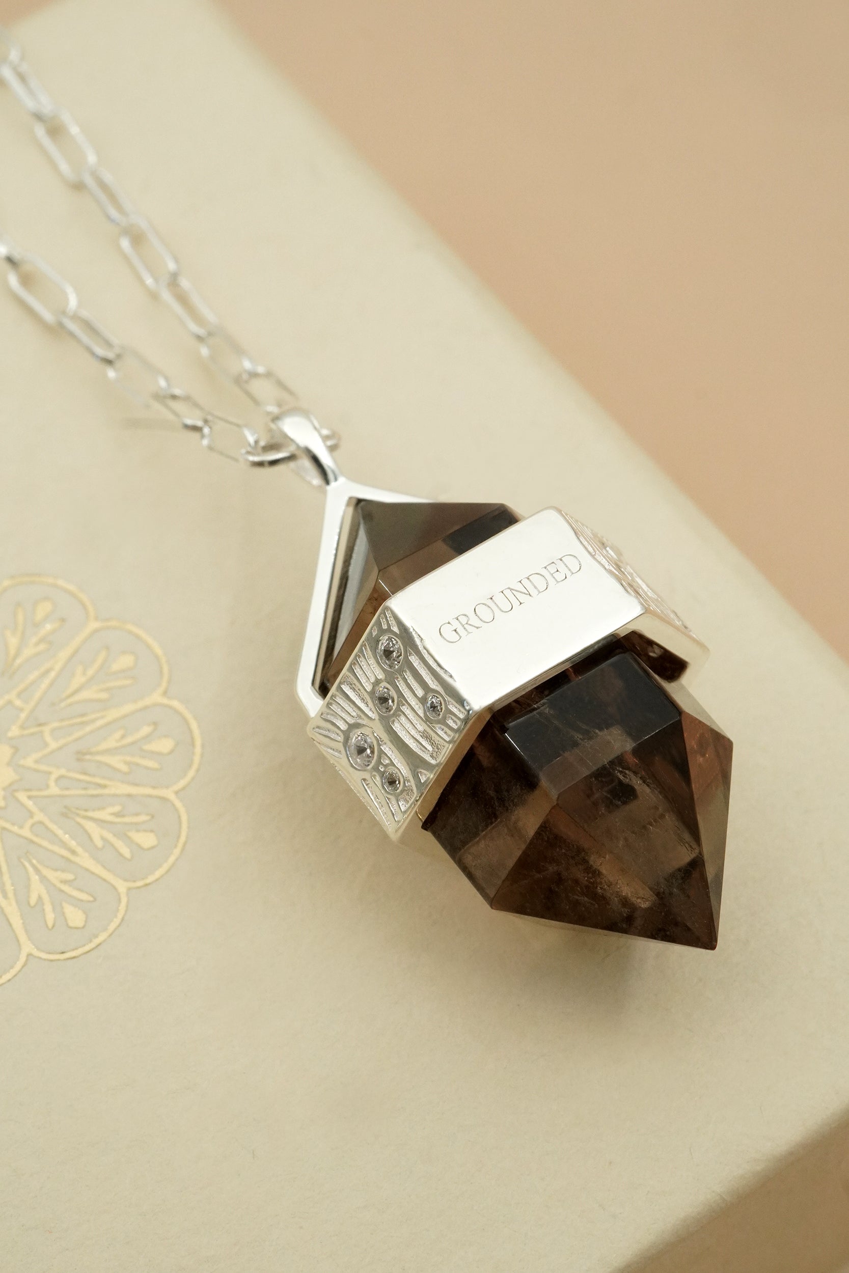 Smoky Quartz pendant necklace for grounding on a cream background.