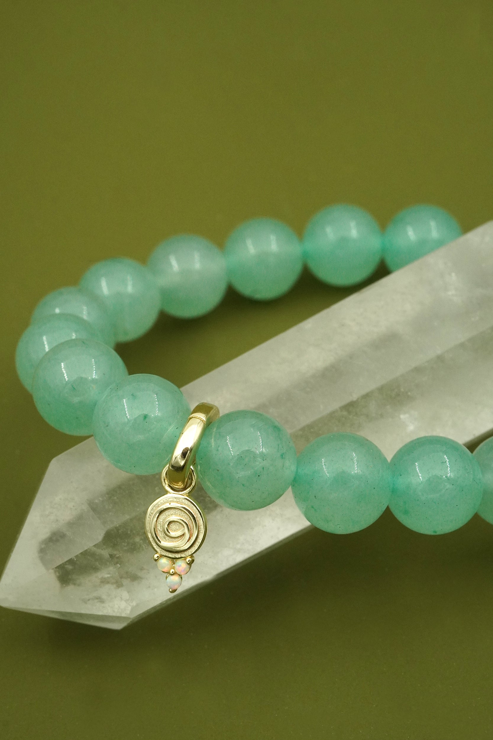 Green aventurine crystal beaded layering bracelet with a gold gratitude charm on a green background