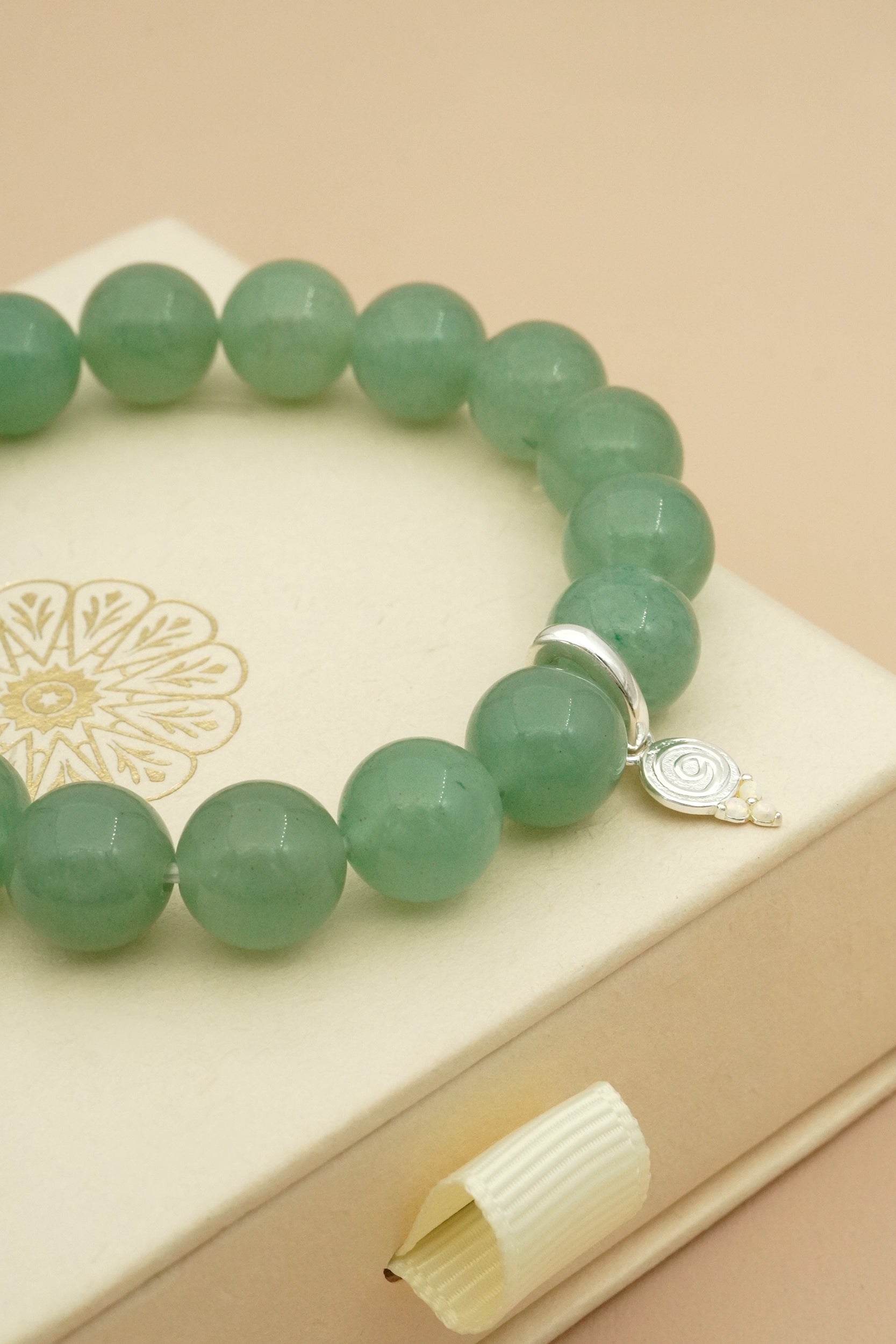 Green aventurine crystal spiritual beaded bracelet with a silver gratitude charm on a beige surface