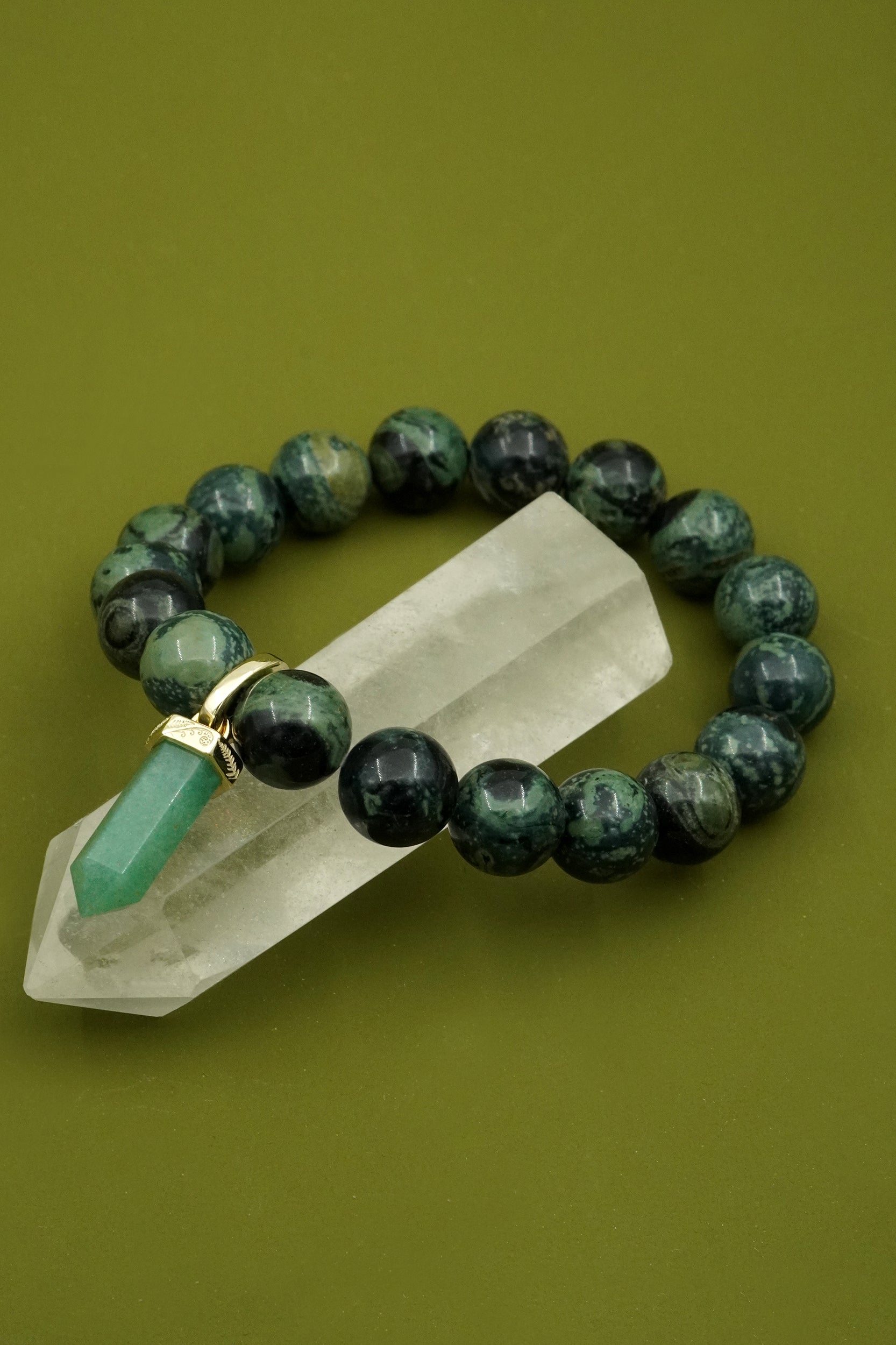 Green beaded gemstone crystal bracelet with a crystal on a green background