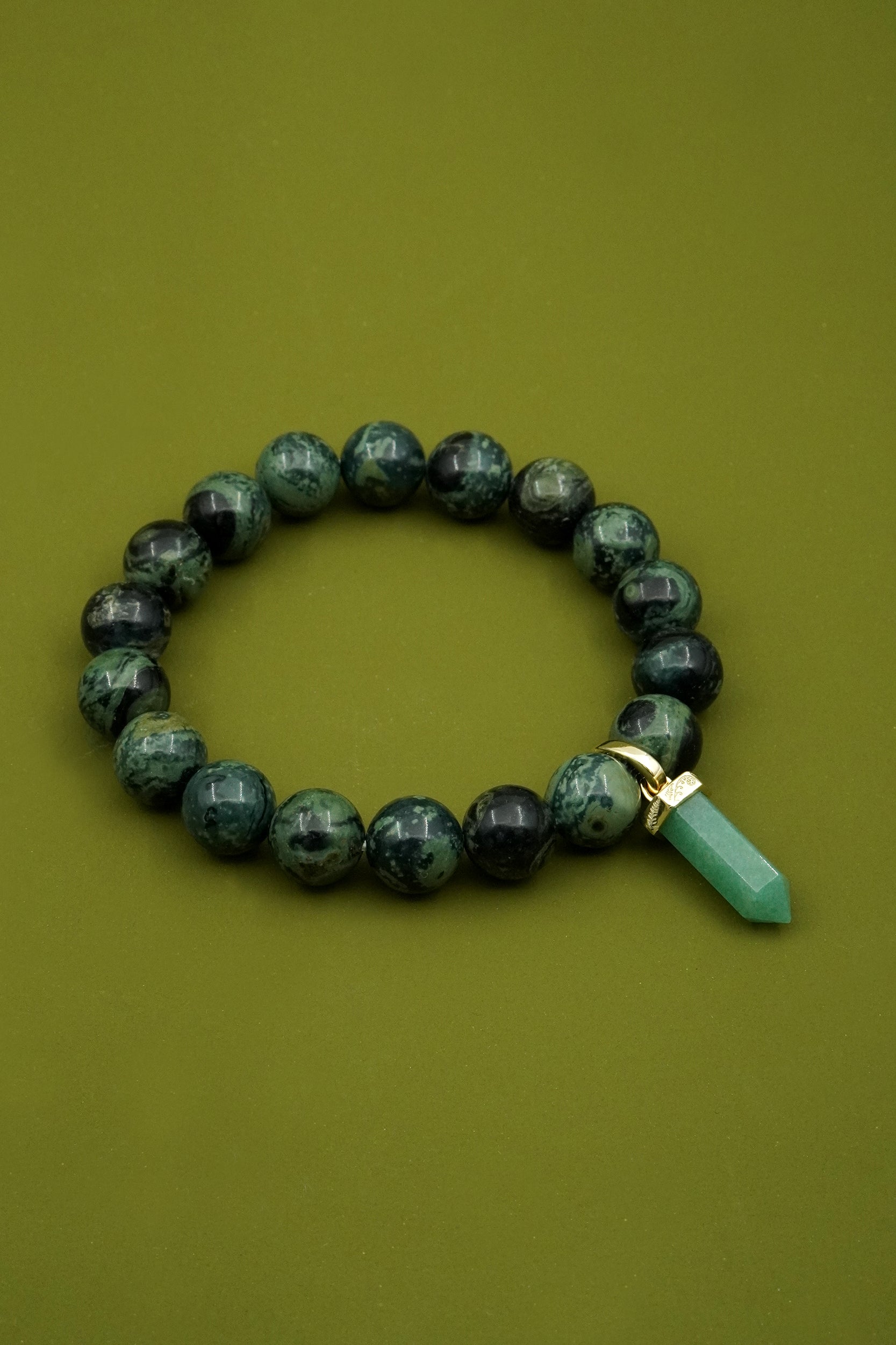 Green beaded crystal bracelet with a gold fern detailed charm  on a green background
