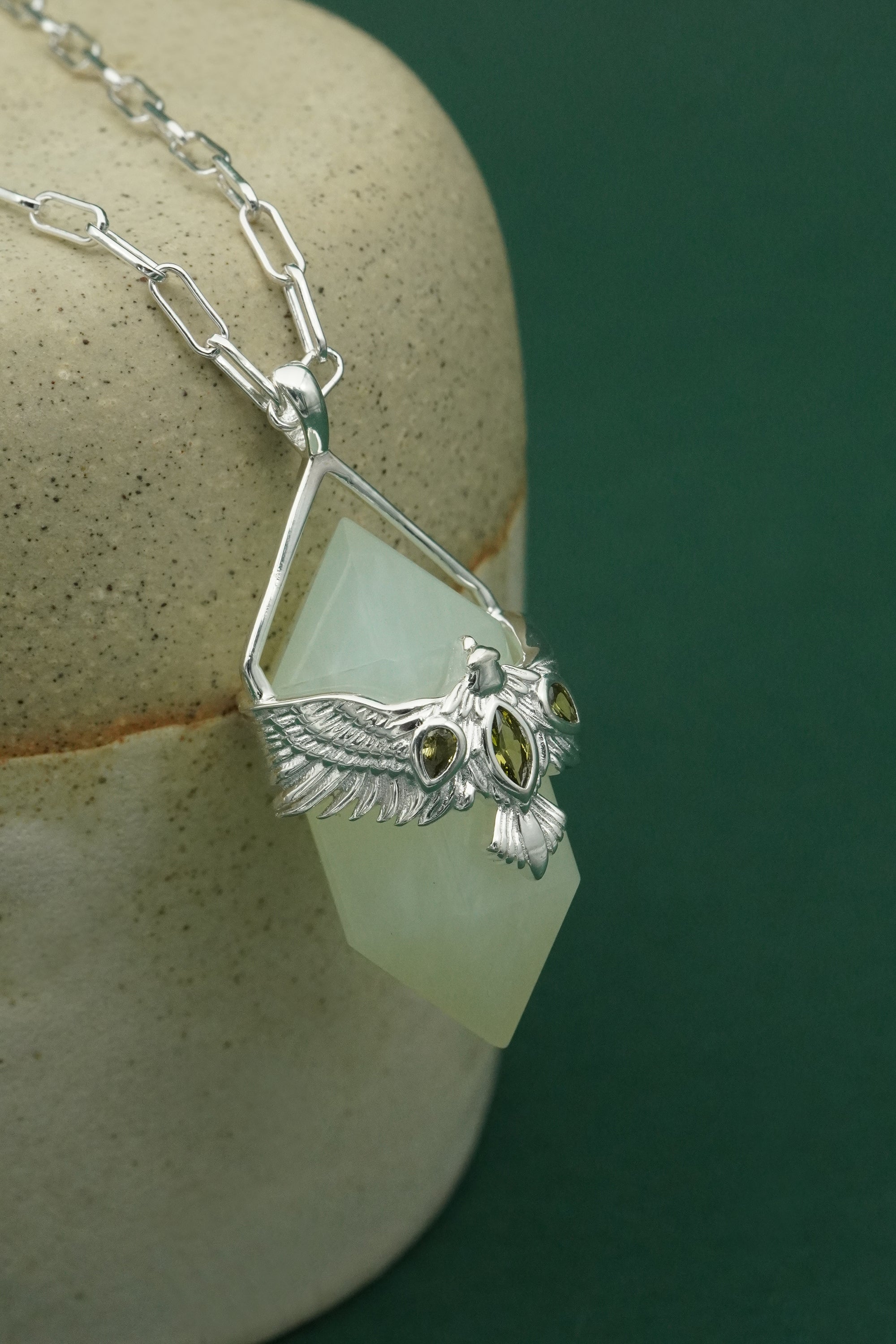 Necklace with a green stone and silver hawk pendant on a neutral background