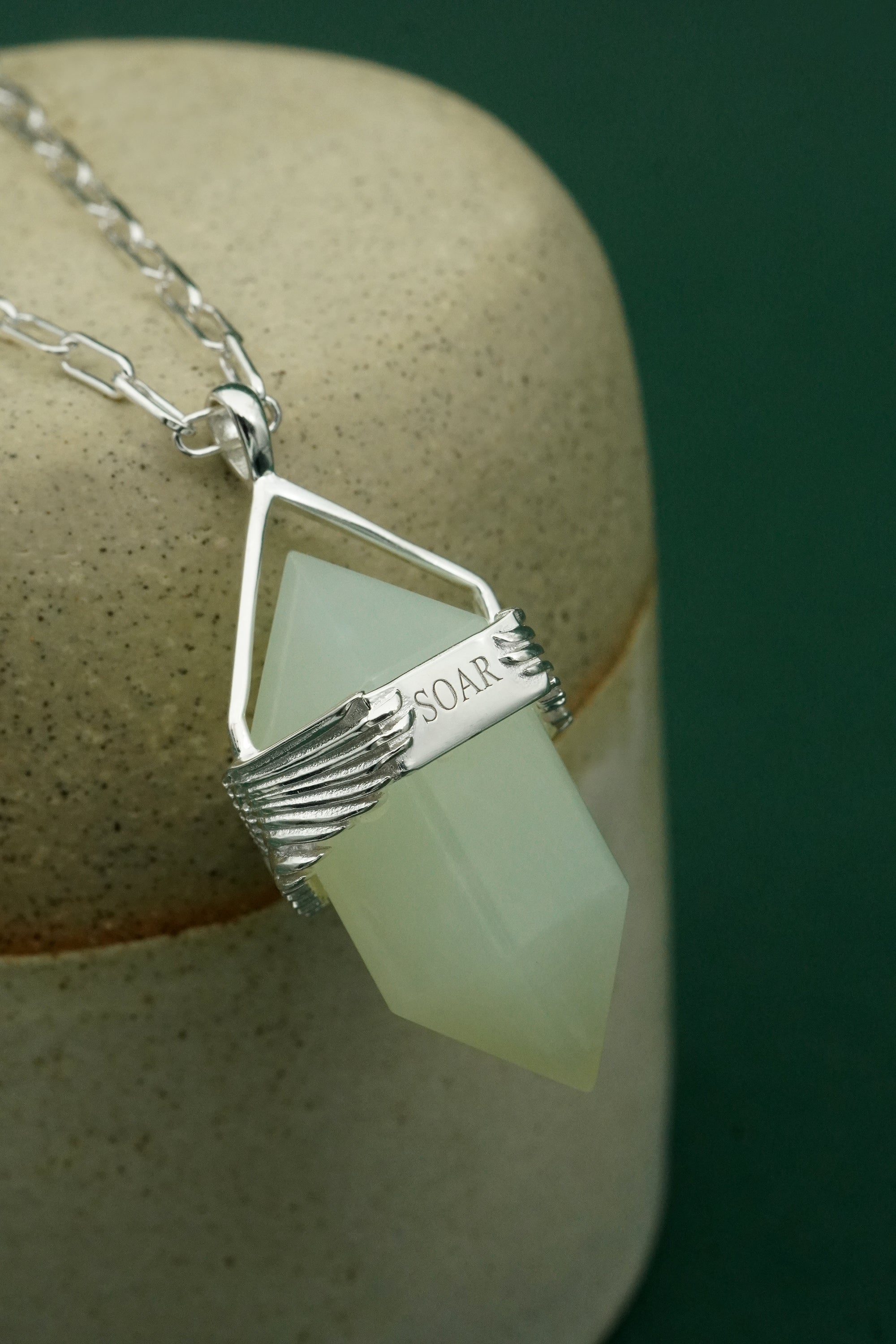 Necklace with a light green gemstone and silver pendant on a beige surface.