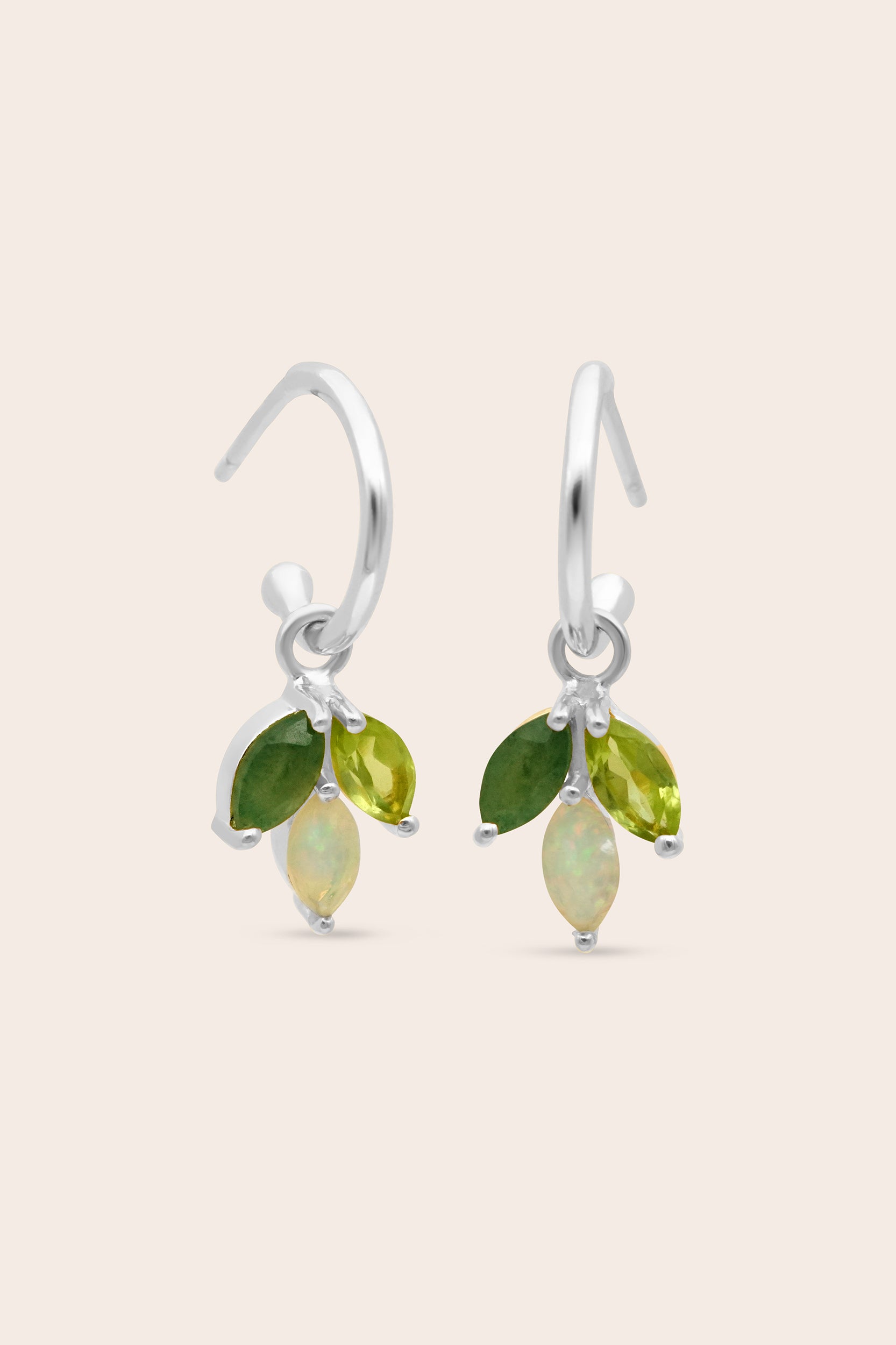 Pair of silver earrings with green and opal gemstones on a beige background