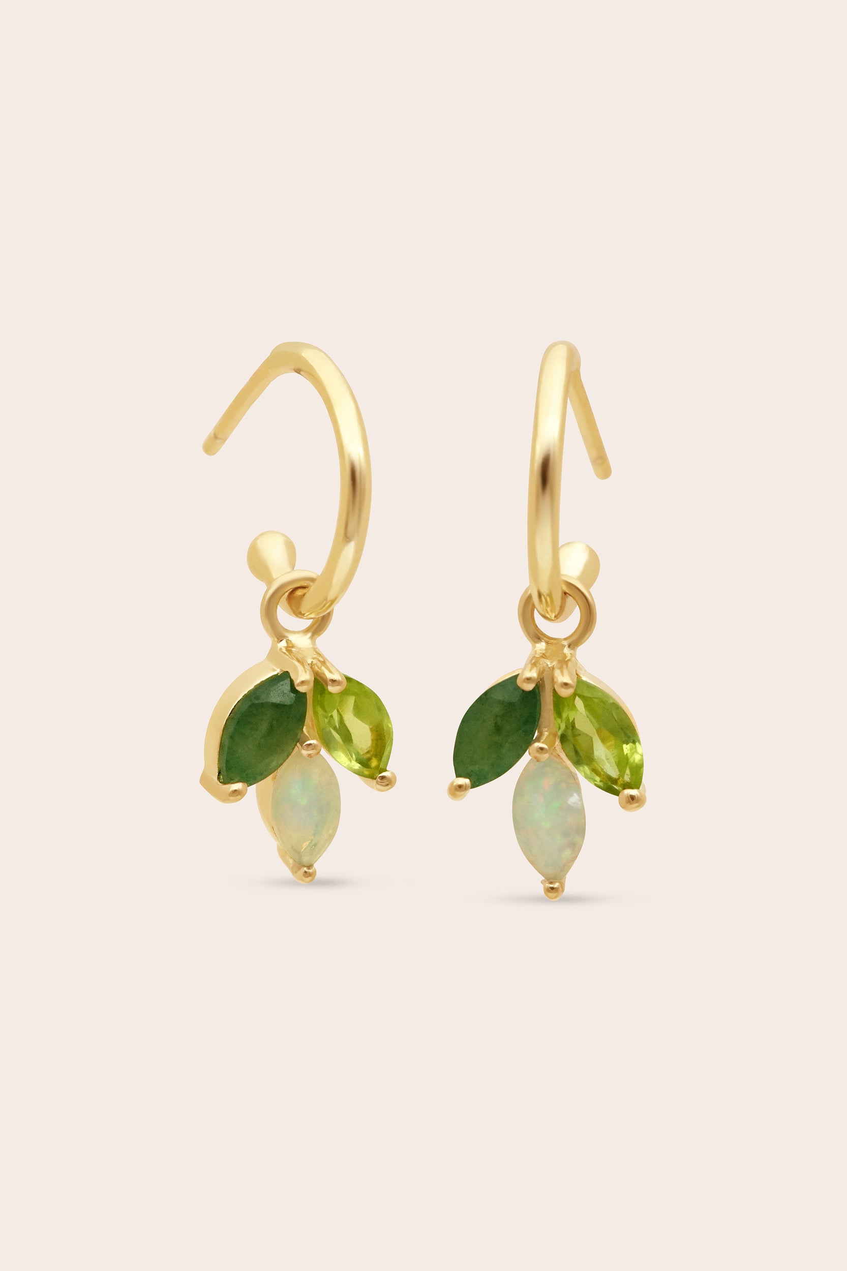 Gold earrings with green and opal stones on a beige background