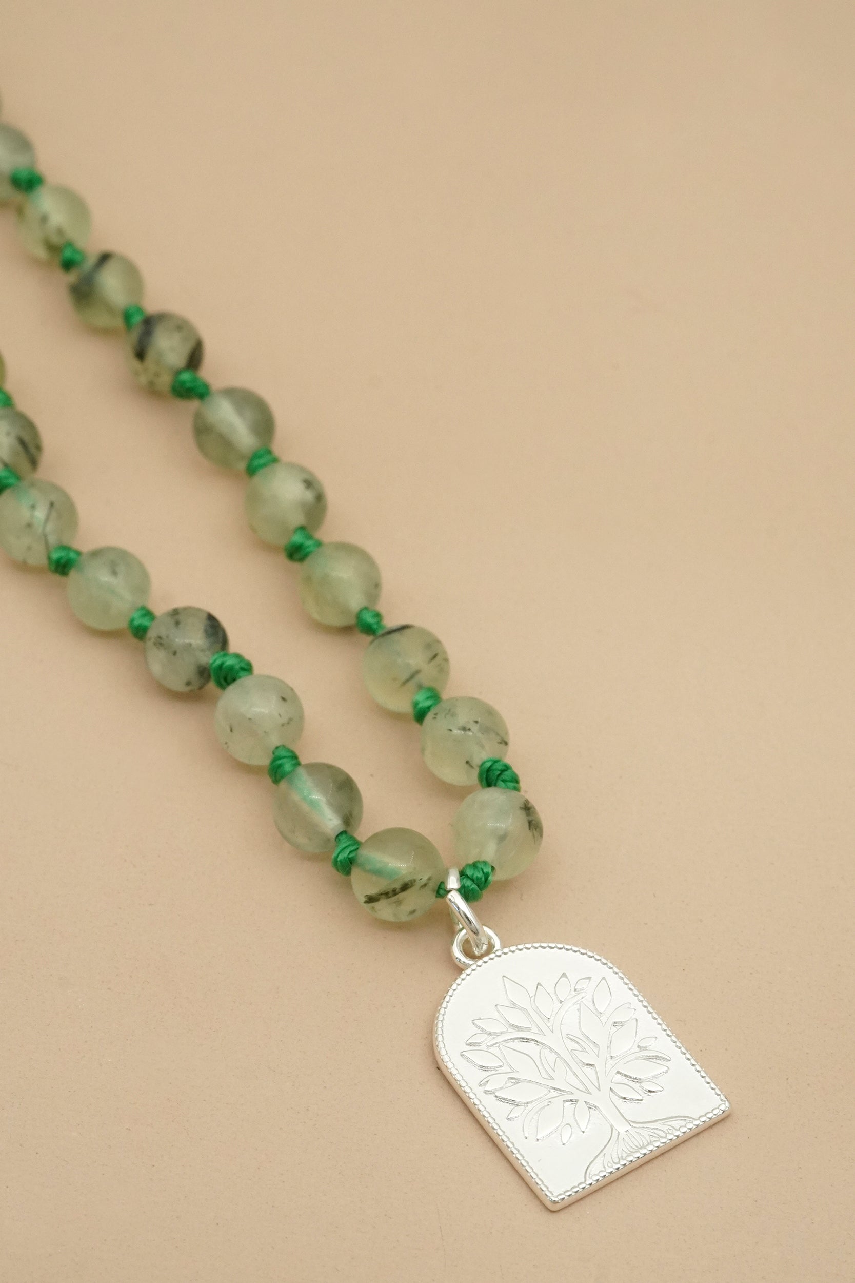 Mala Necklace with green beads and a silver tree pendant on a beige background