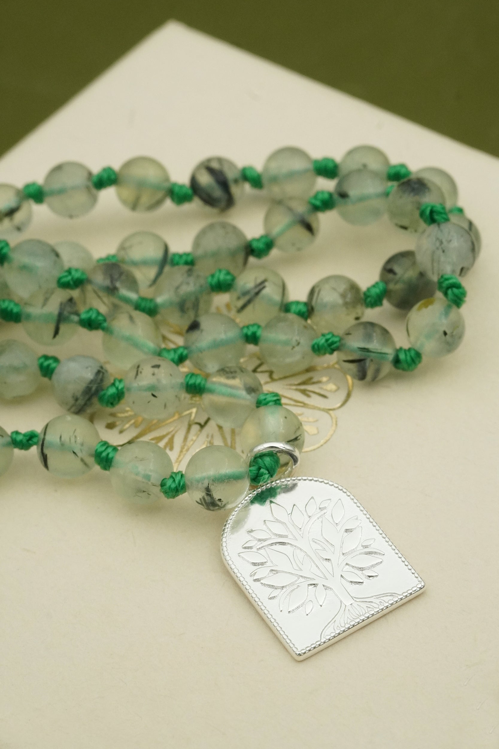 Green beaded prayer male necklace with a silver tree of life pendant on a beige surface
