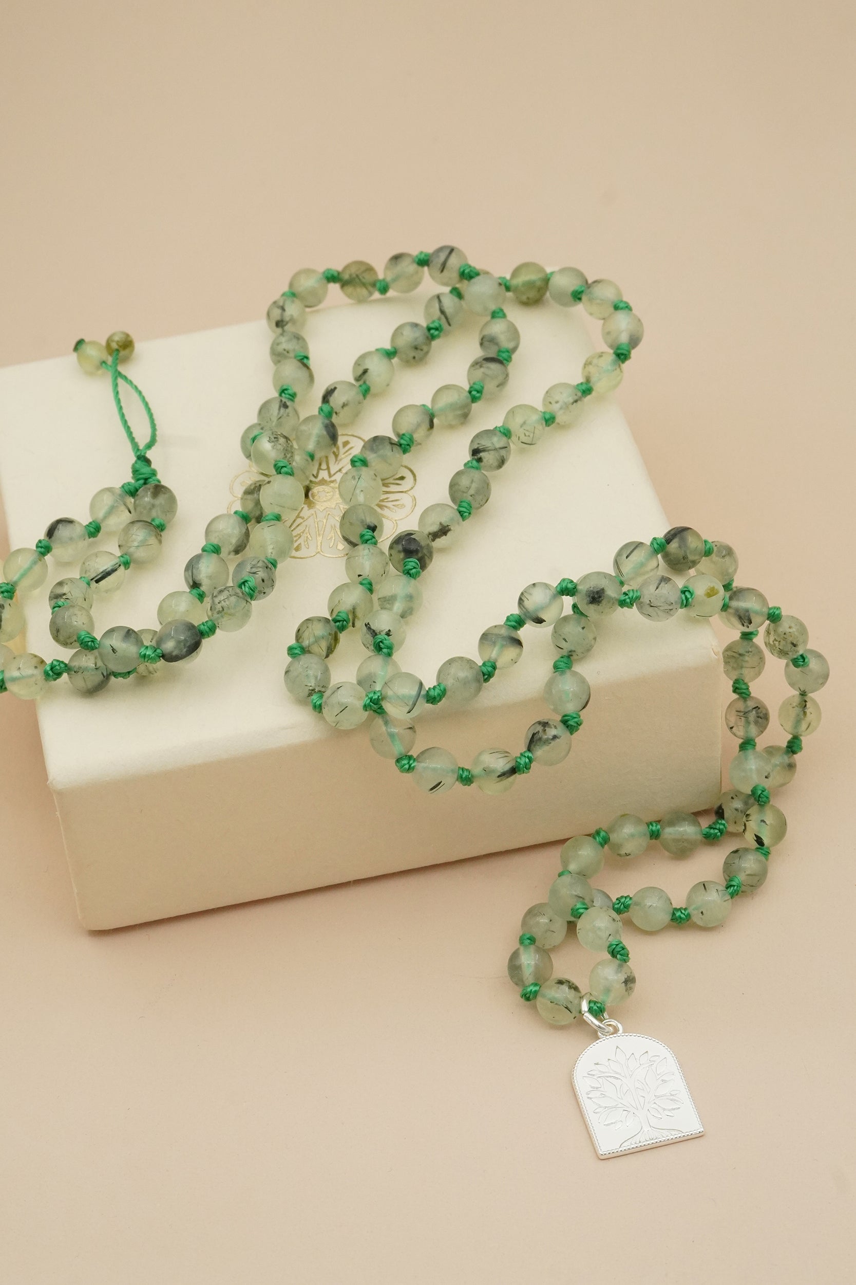 Green beaded male necklace with a silver tree of life pendant on a beige surface