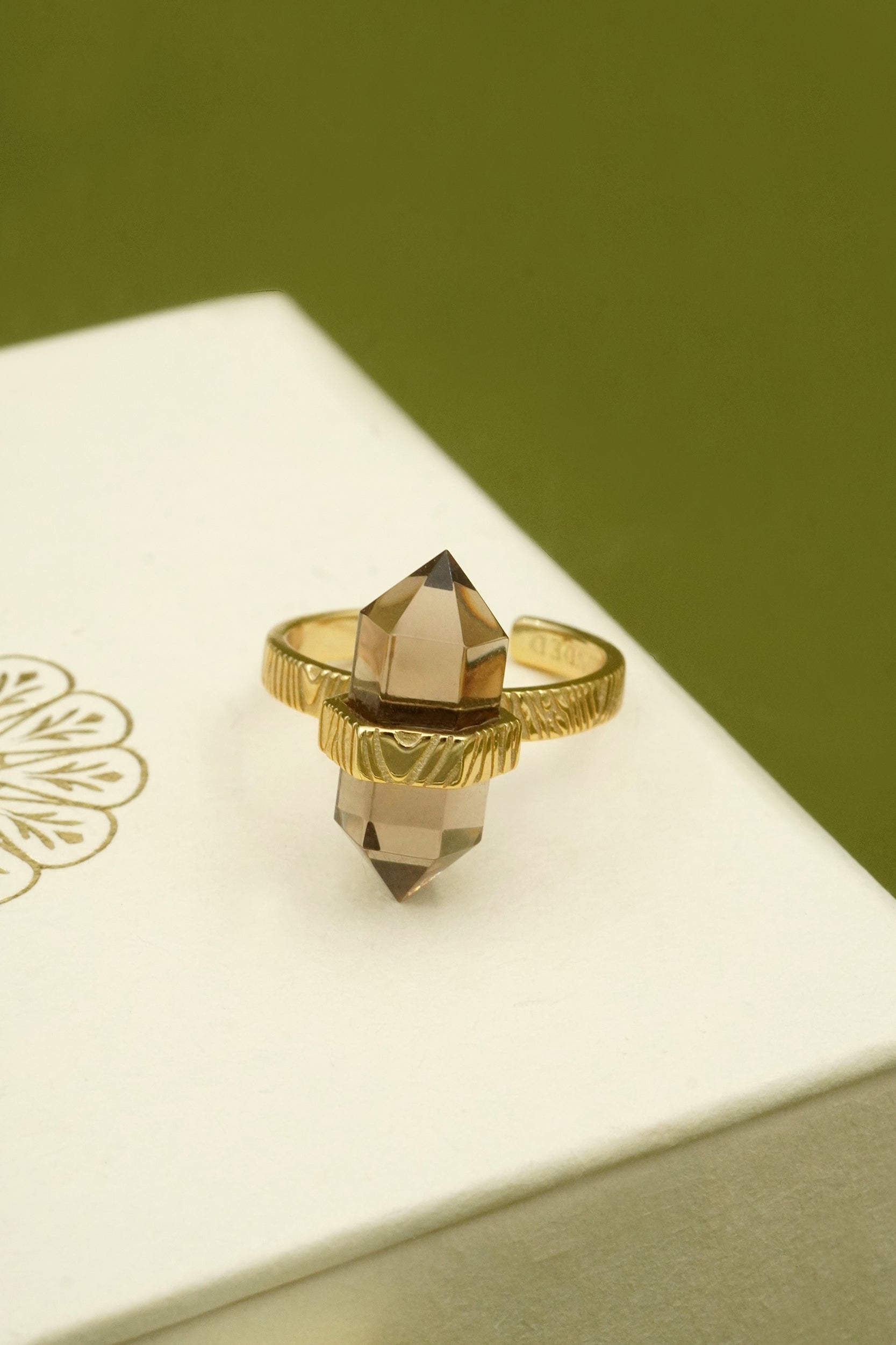 Gold ring with a crystal on a white box with gold design