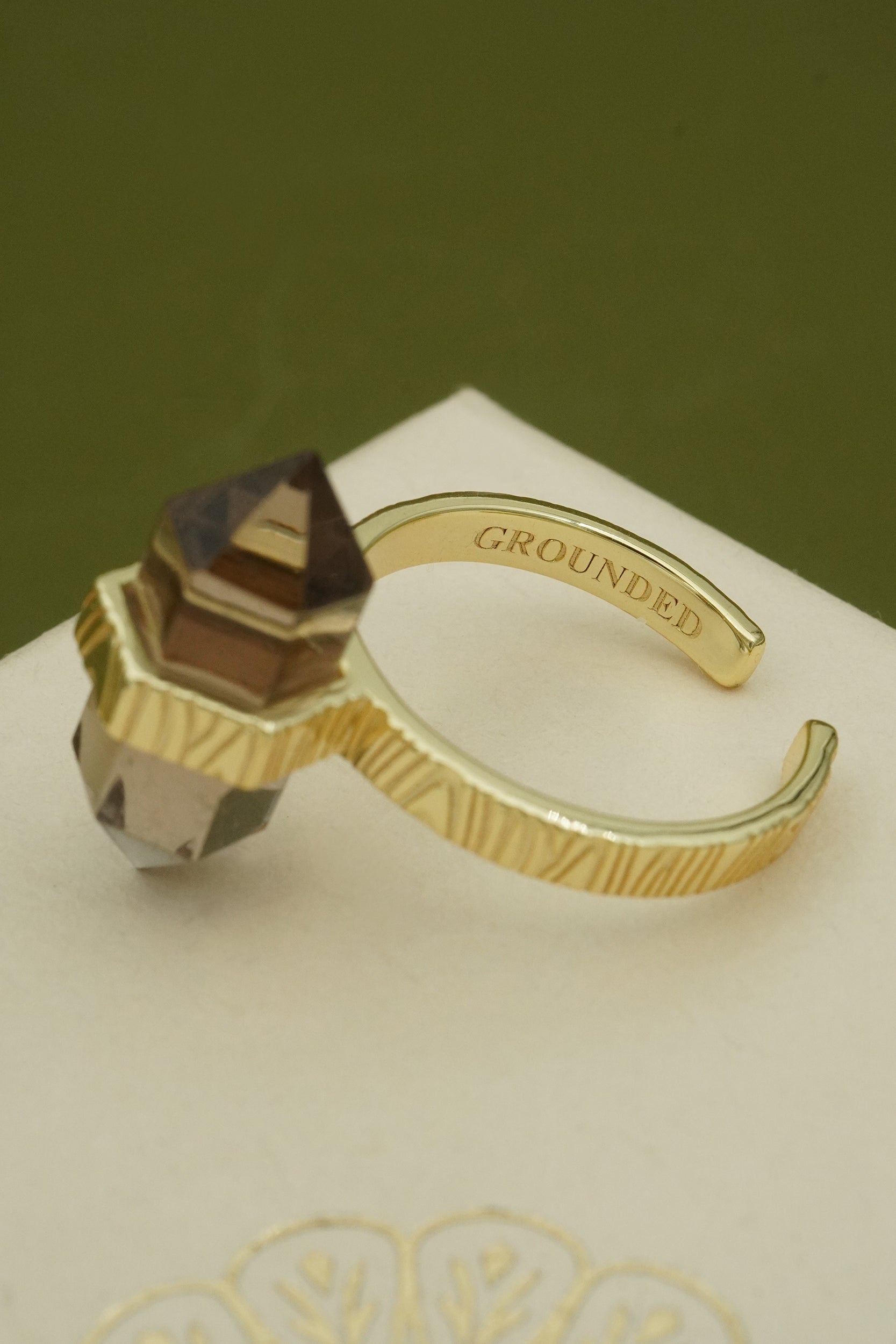 Gold ring with geometric design on a white surface with 'GROUNDED' text.