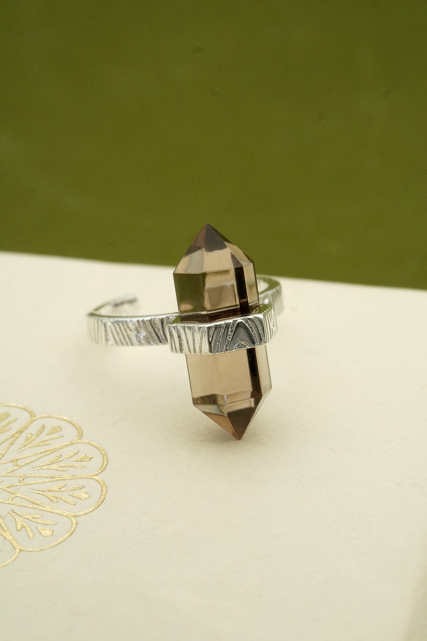 Silver ring with a smoky quartz crystal on a green and beige background
