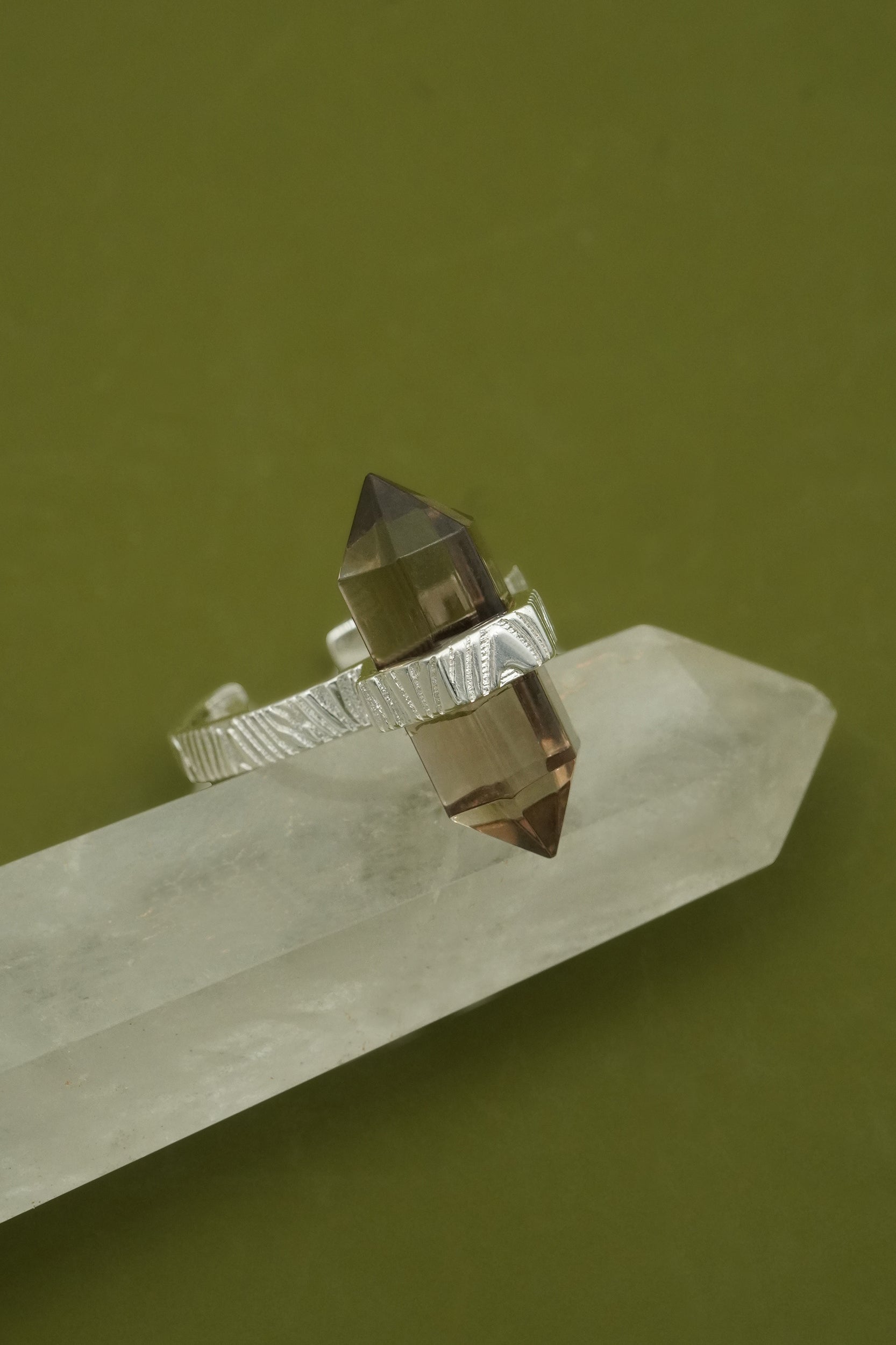 Crystal ring with a metallic prong on a crystal base against a green background