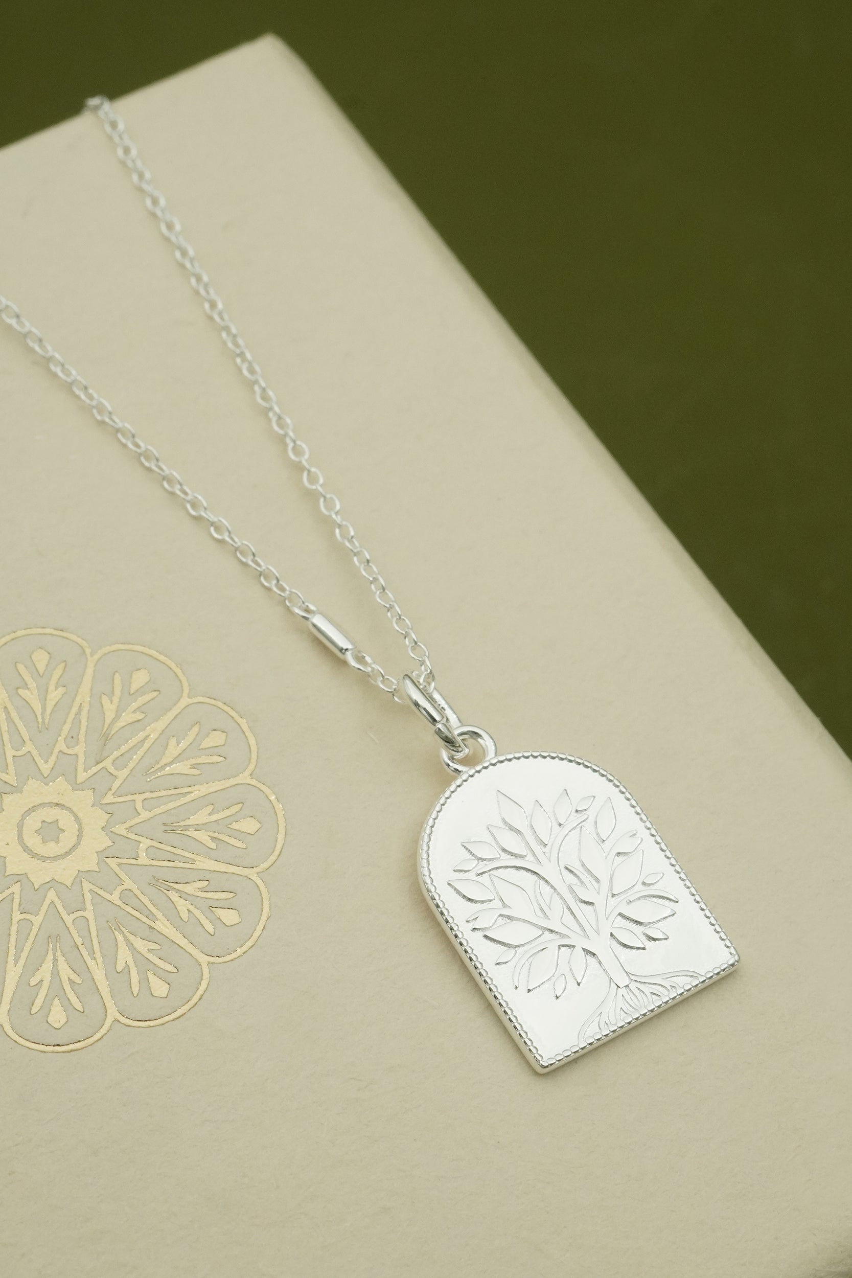 Silver necklace with an embossed tree pendant on a beige surface