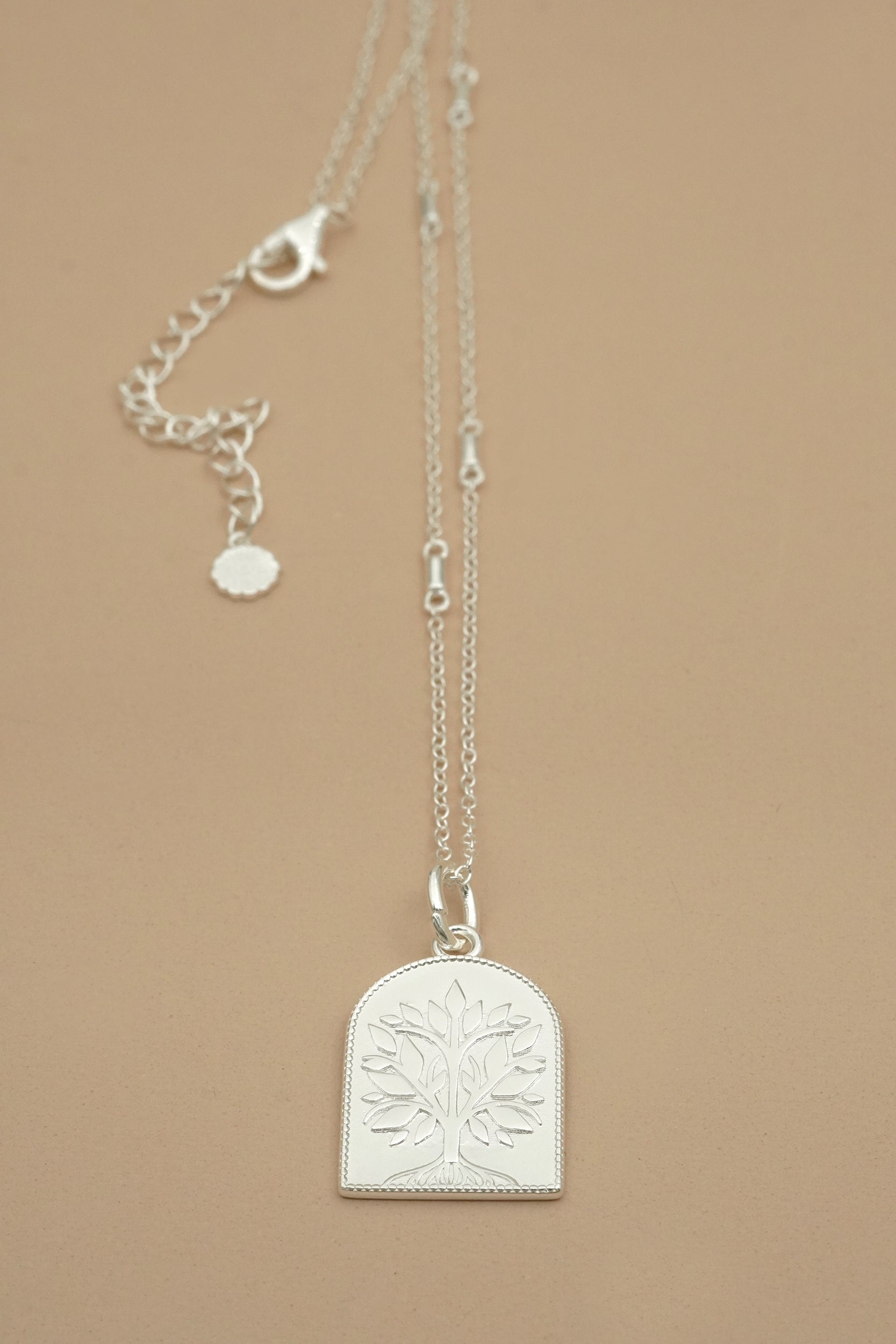 Silver necklace with a tree-of-life pendant on a beige background