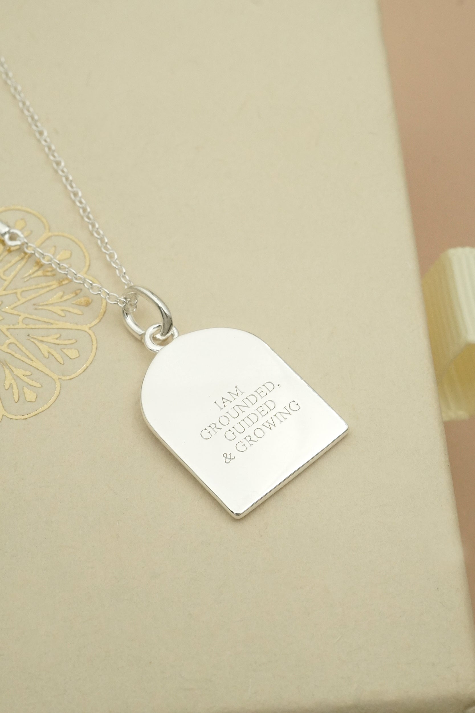 Silver necklace with inscription I am grounded, guided and growing on a beige background