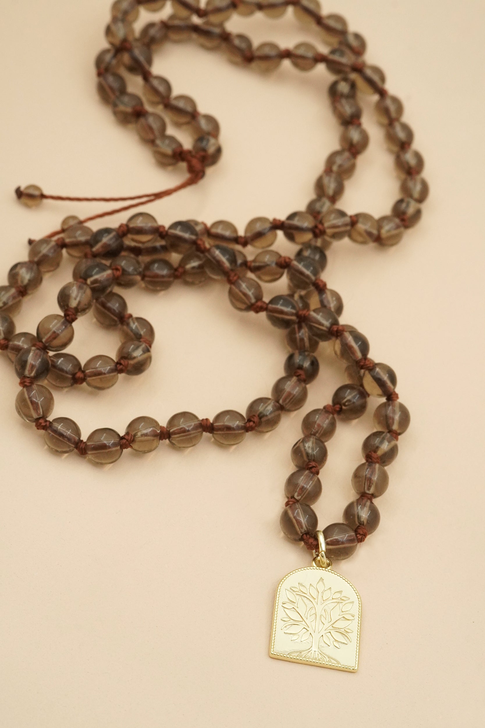 Brown beaded male necklace with a gold tree of life pendant on a beige background