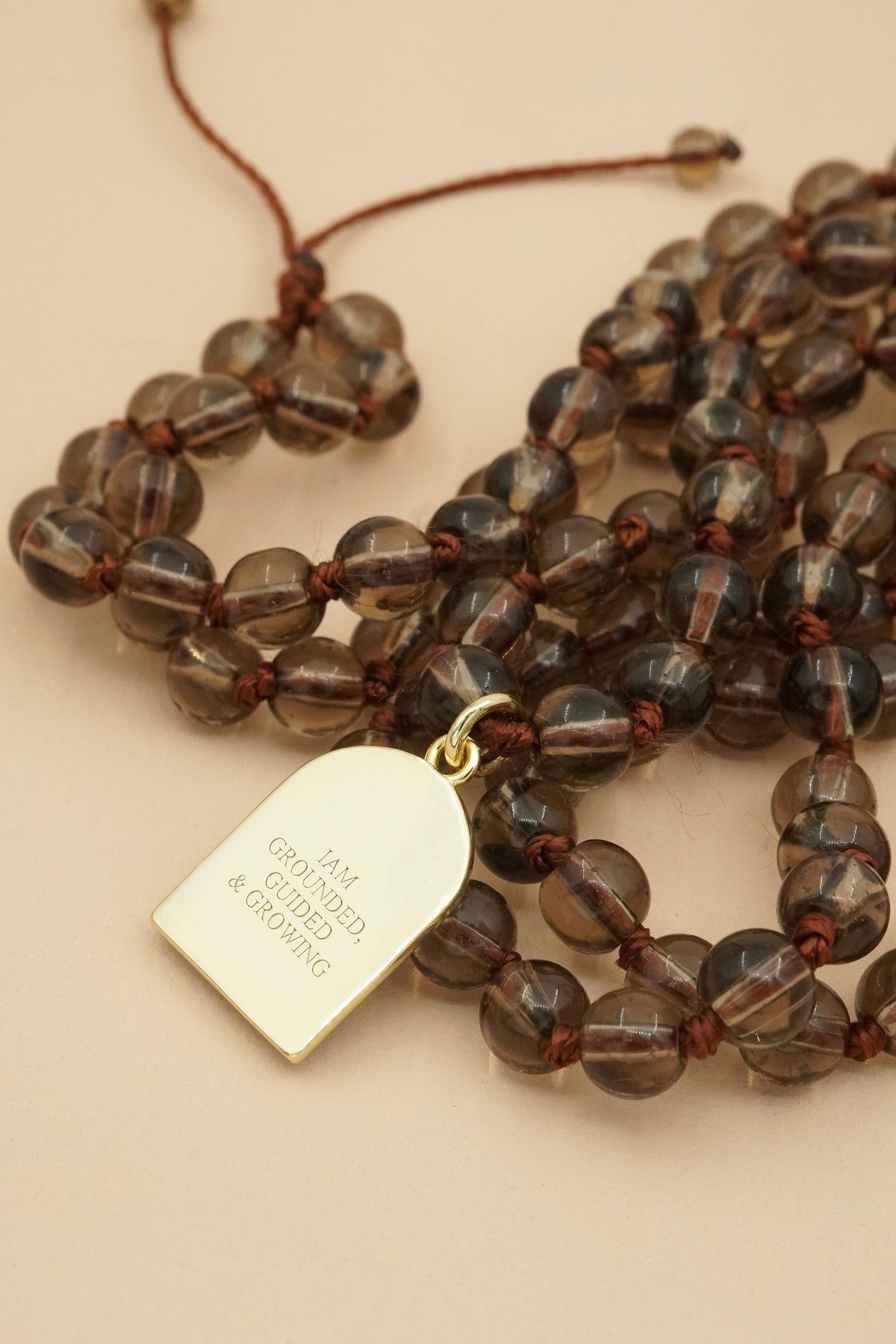Mala Necklace with smoky quartz brown beaded male necklace and gold pendant on a beige background