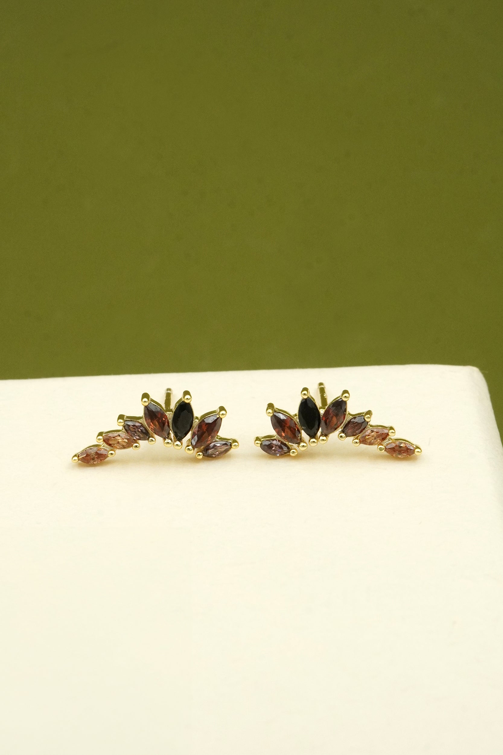 Pair of gold climber earrings with gemstones on a white surface with a green background