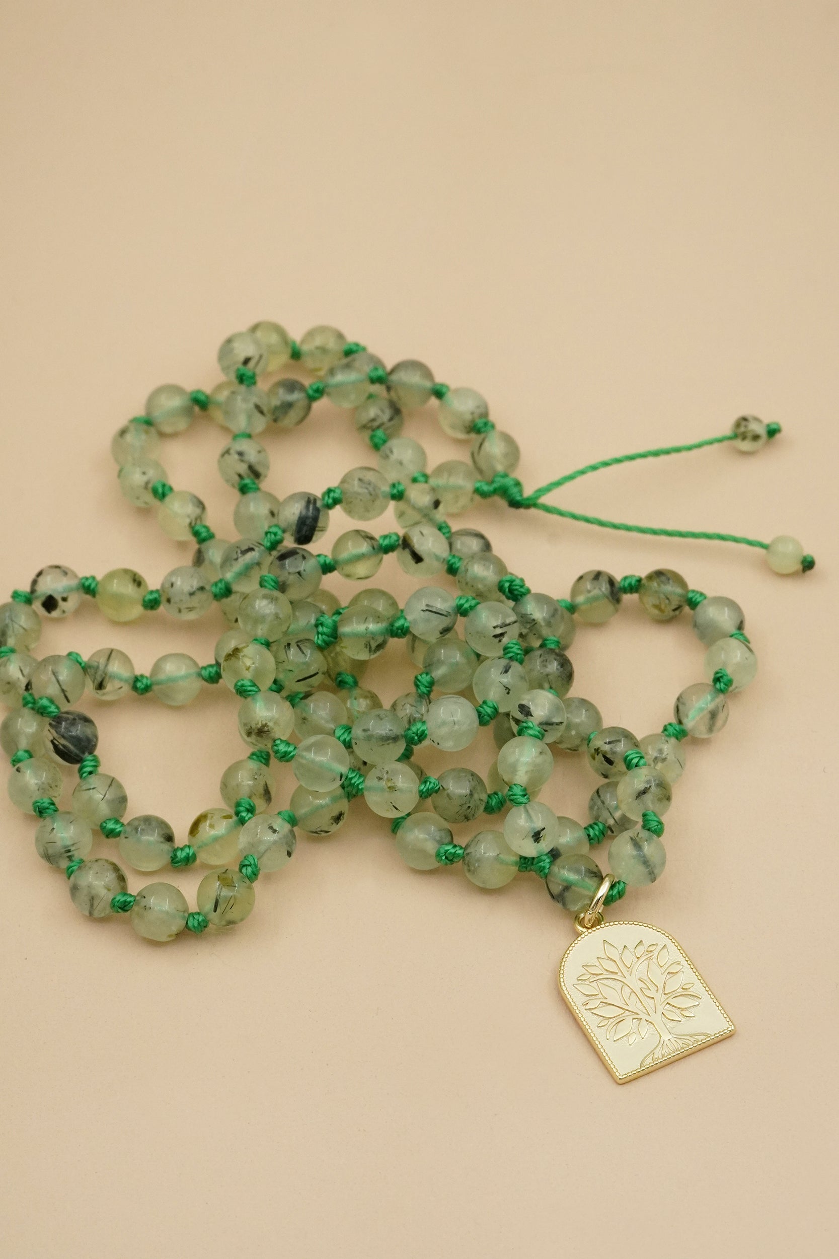 Green beaded male necklace with a gold tree of life pendant on a beige background