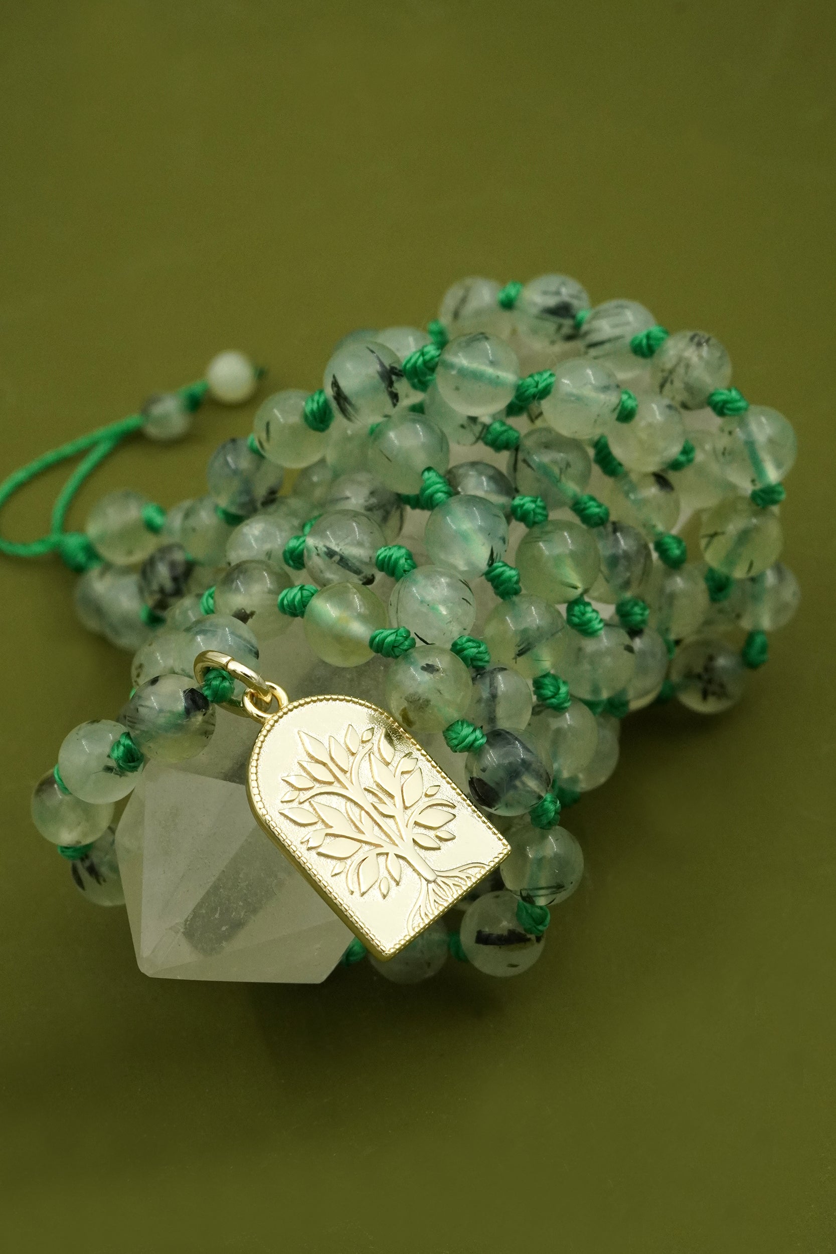 Necklace with green mala beads and a gold tree of life pendant on a green background