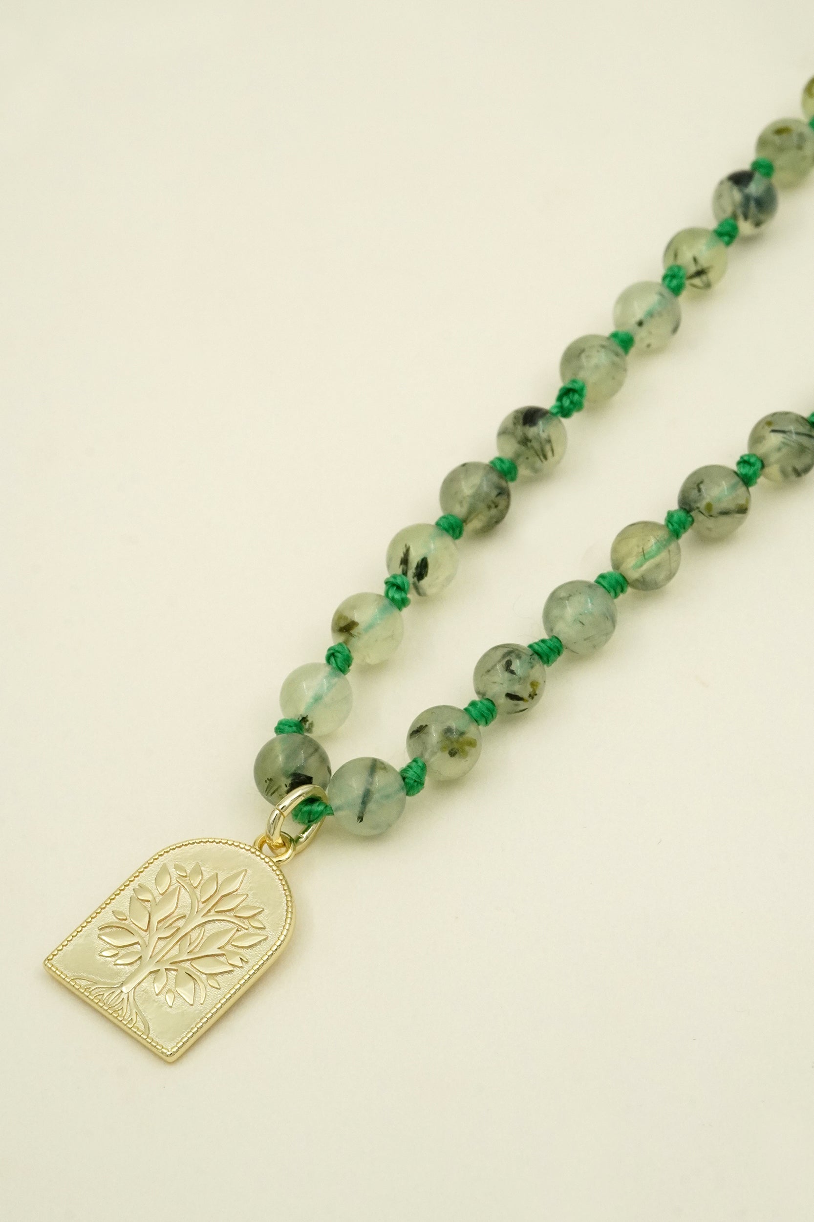 Necklace with green mala beads and a gold tree pendant on a beige background