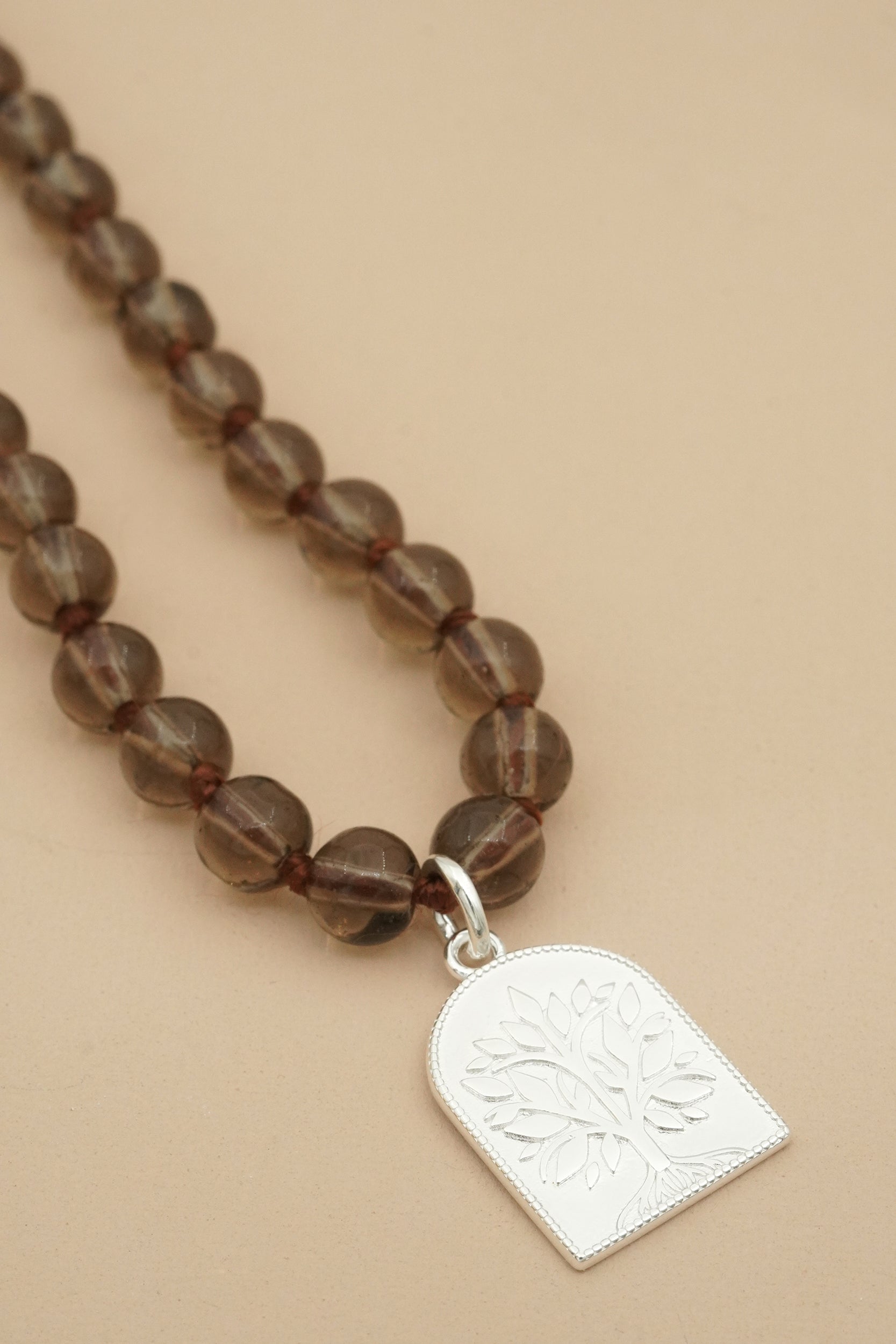 Brown beaded male prayer necklace with a silver tree of life pendant on a beige background