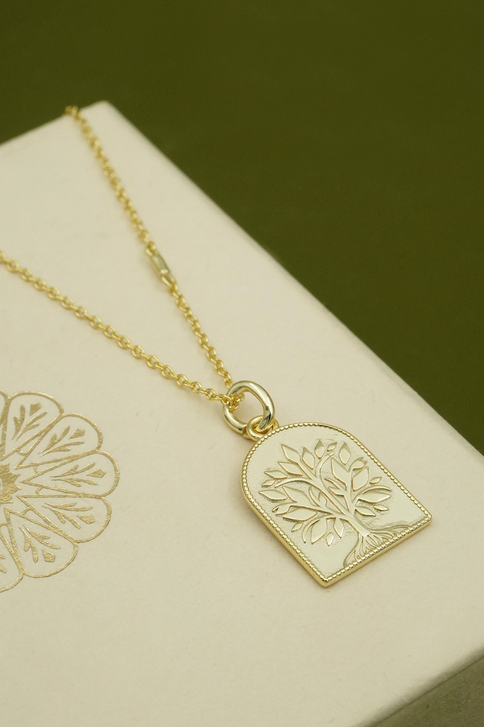 Gold necklace with a tree-of-life pendant on a beige box with floral design